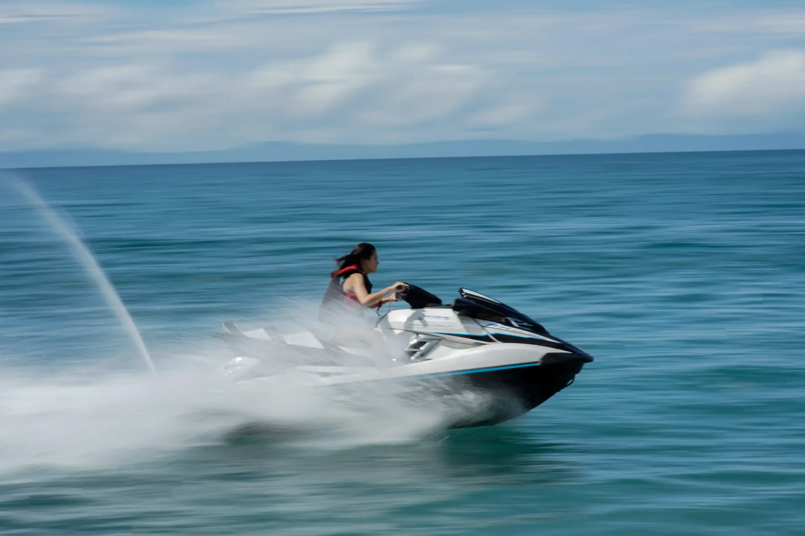 Woman riding a jet ski at high speed across blue ocean waters.