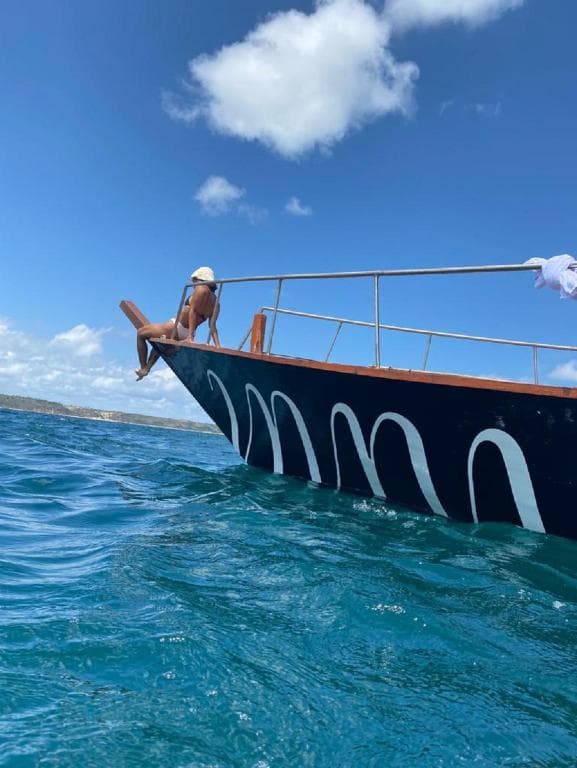 Low-angle view of a person relaxing on the bow of a wooden boat sailing through clear blue ocean waters.