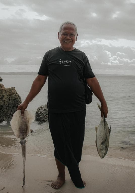 Smiling local fisherman standing on the beach holding a freshly caught squid and fish.