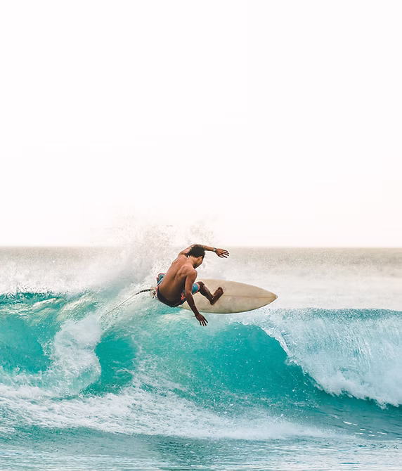 A male surfer riding a clear turquoise ocean wave as it curls and sprays water.