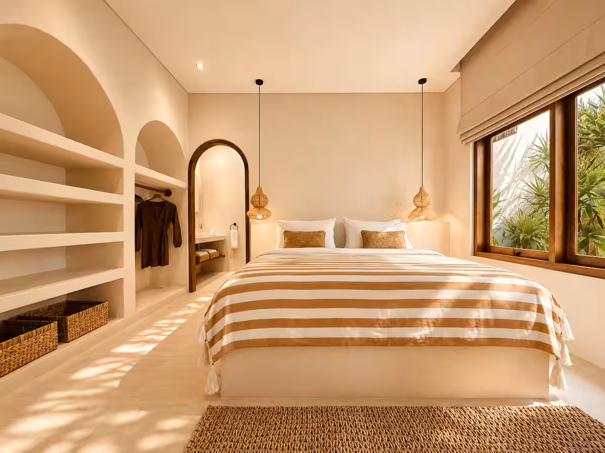 Spacious master bedroom with built-in arched wall shelving, hanging rattan pendant lights, and a striped bed facing a garden view.