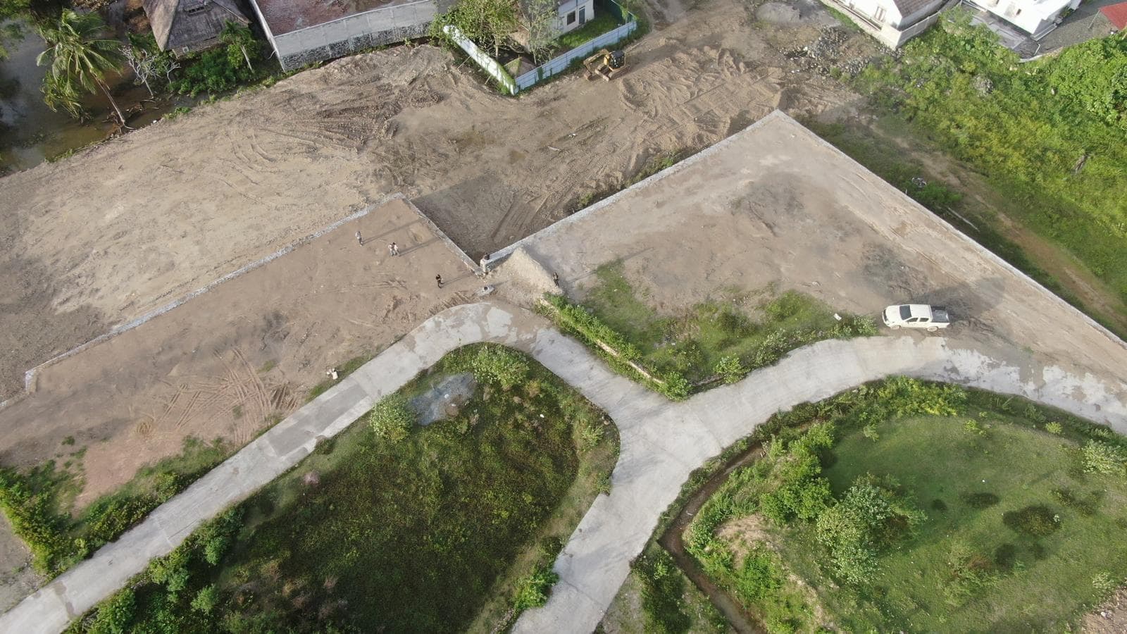 Elevated corner plot of cleared development land secured by a large stone retaining wall, with a white pickup truck parked nearby.