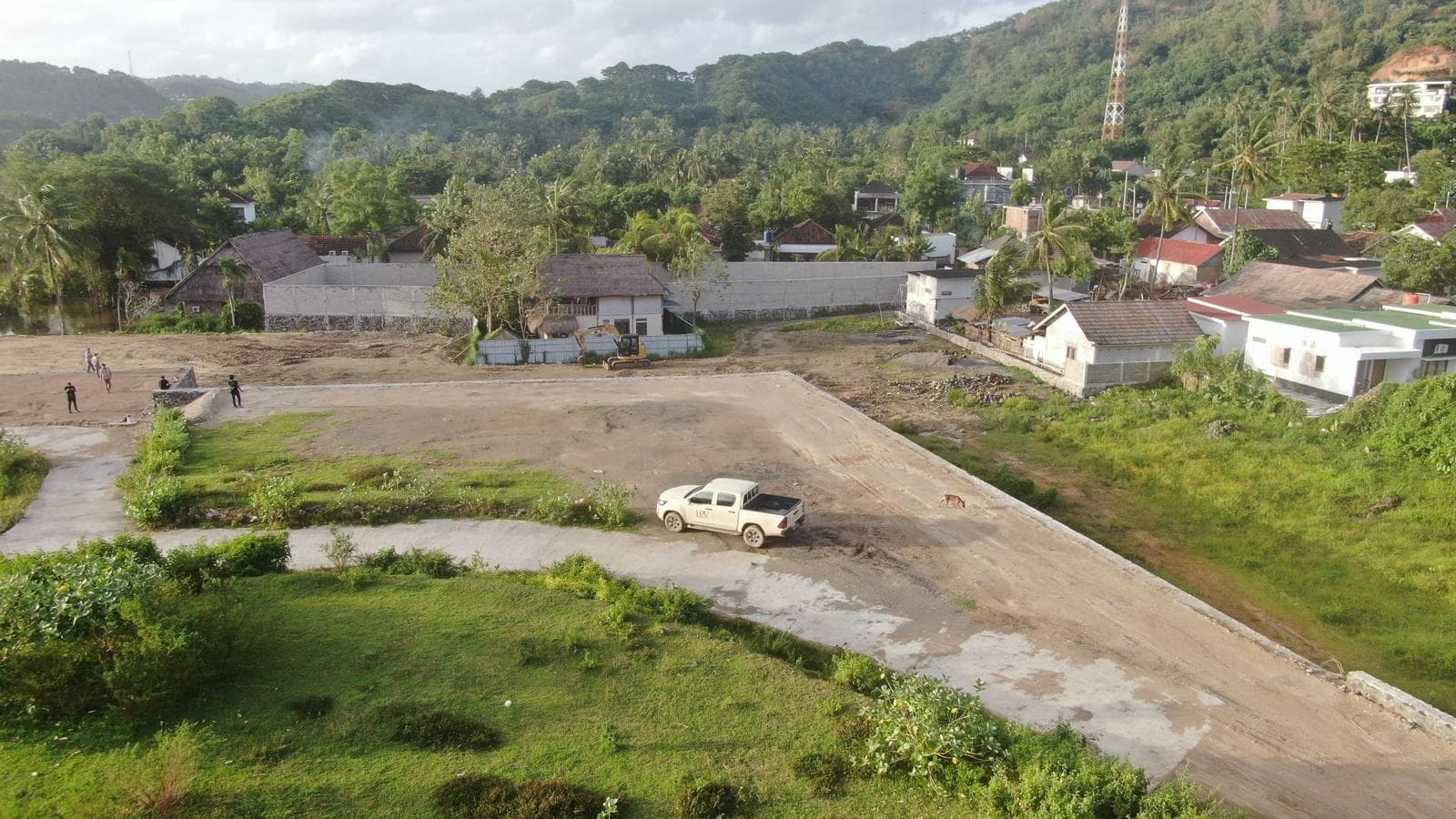 Ground-level aerial perspective of the plot facing green hills and nearby local residential buildings.