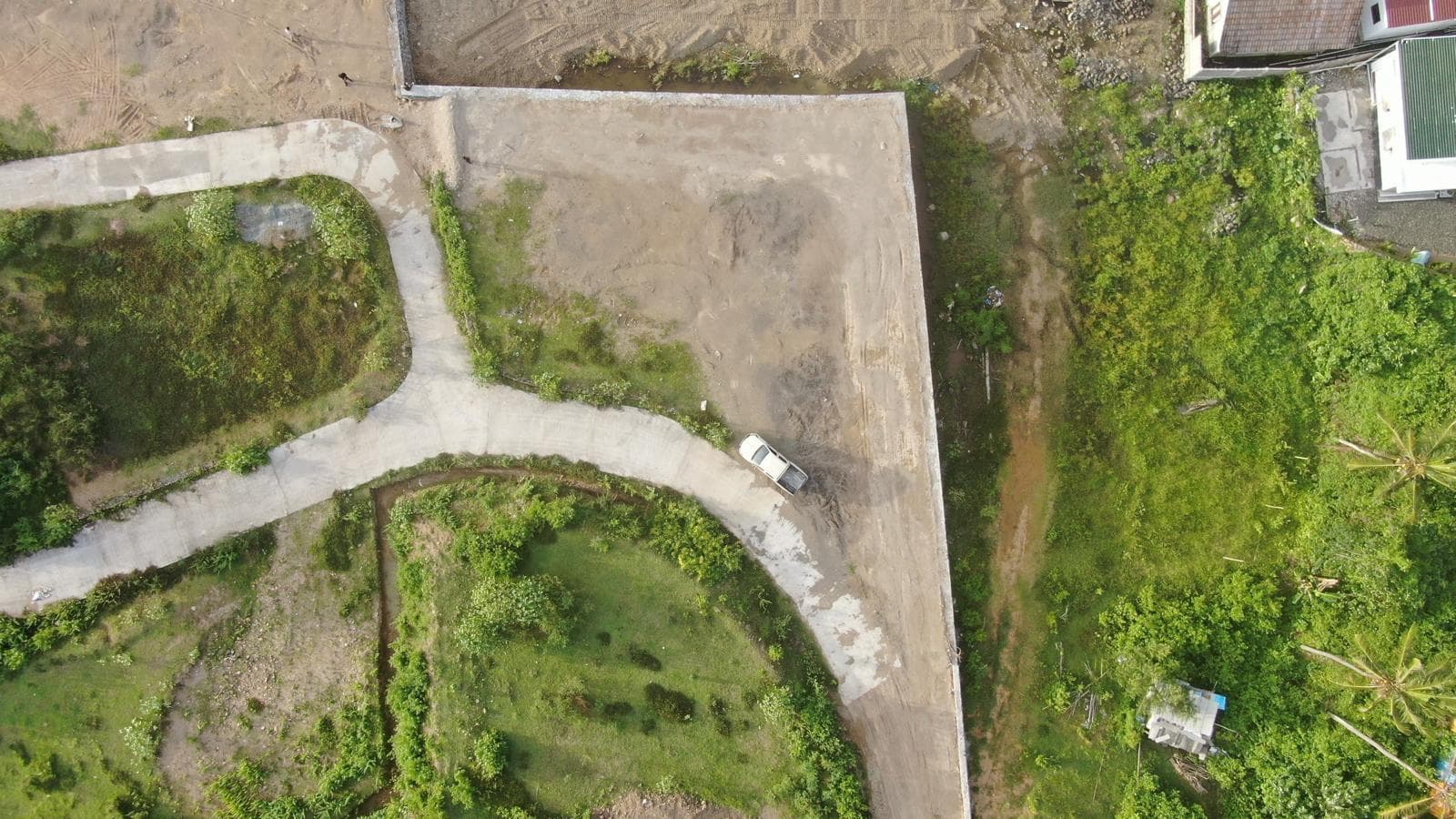 Direct overhead view of the land plot, highlighting the curved internal road and surrounding natural terrain.