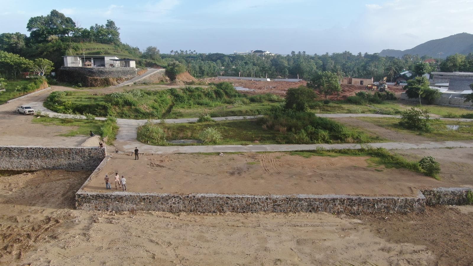 Wide shot showing the stone foundation wall of the plot with open land and hills in the background.