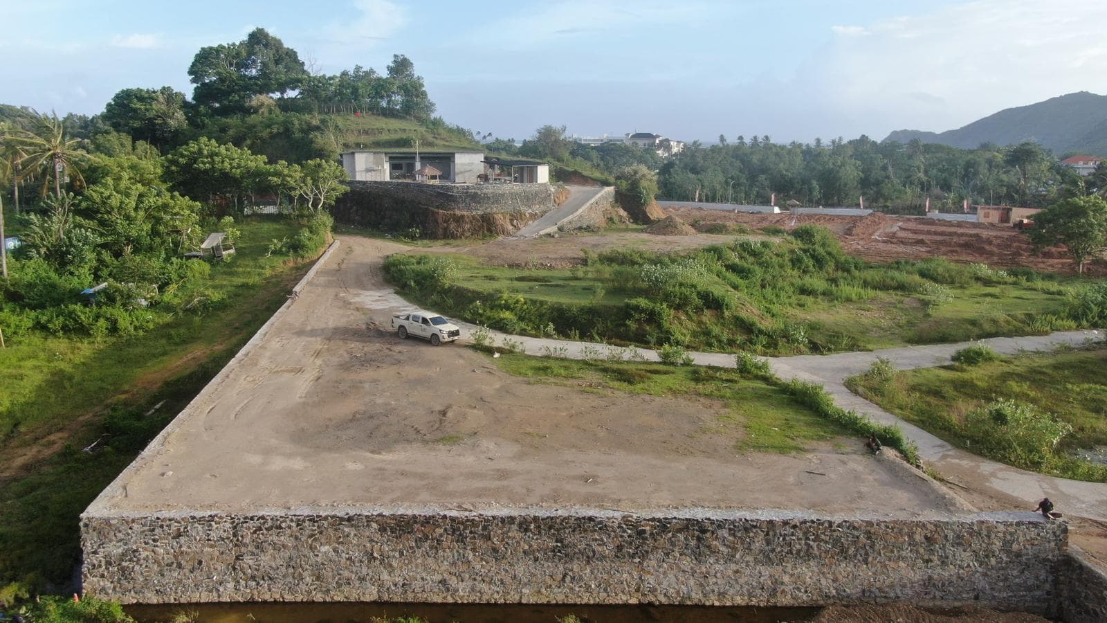 Side angle of the elevated land parcel, showing the thick retaining wall along the road access.