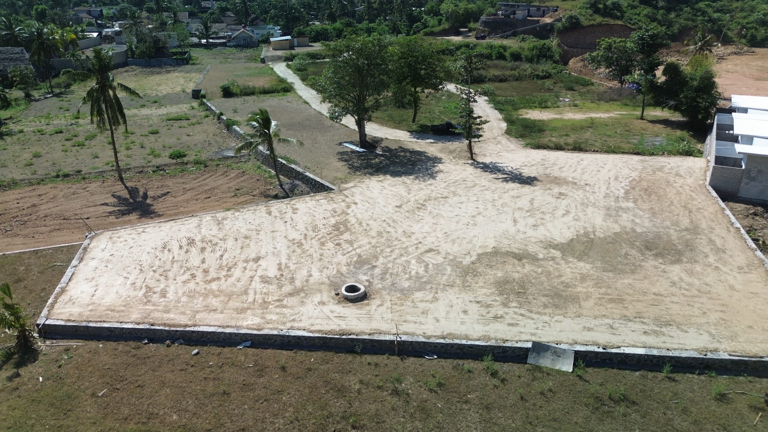 Low-angle drone view of a cleared, level land plot bordered by a stone wall.
