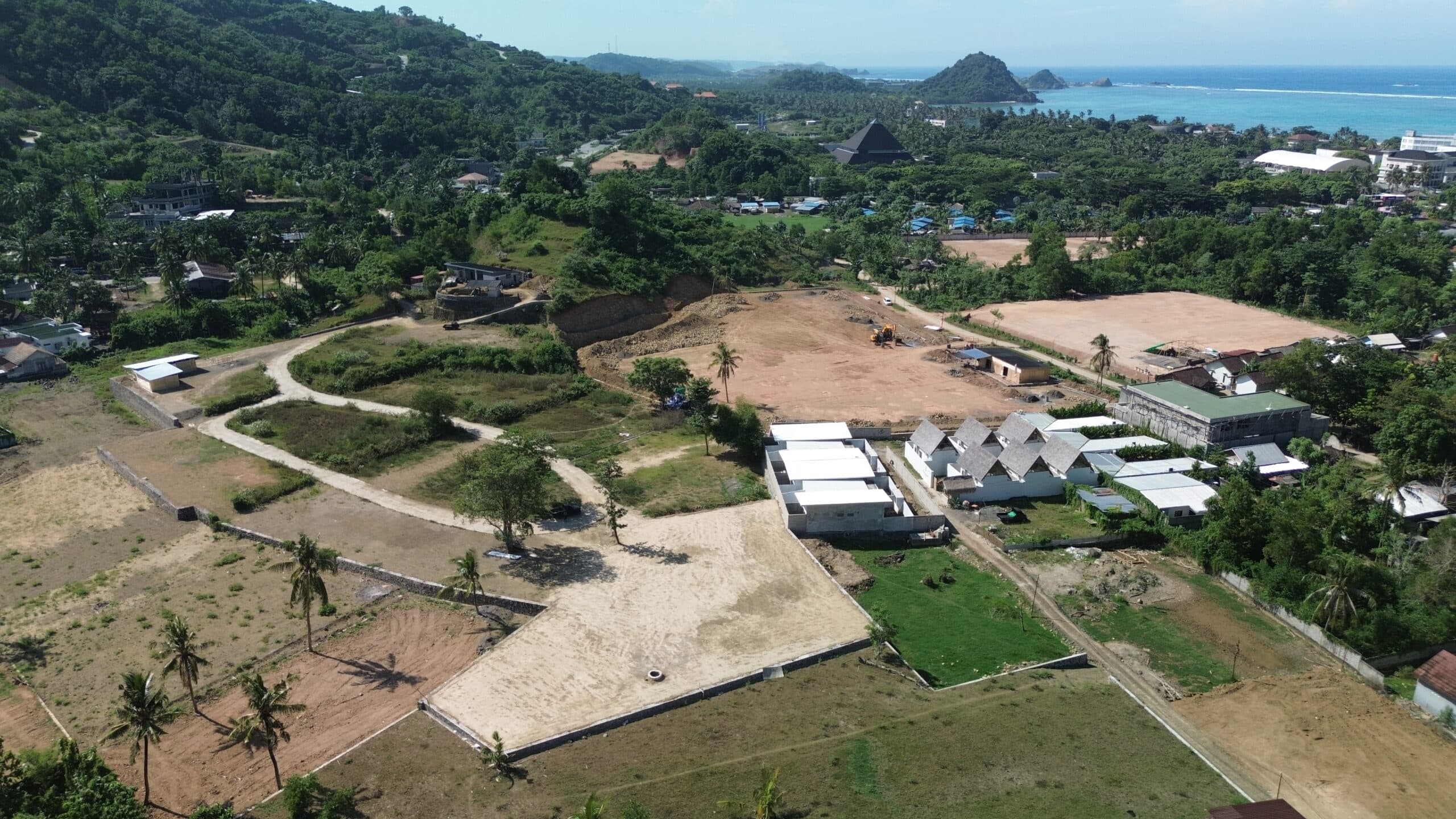 High-angle aerial view of the development plot showing surrounding greenery and coastal ocean in the background.