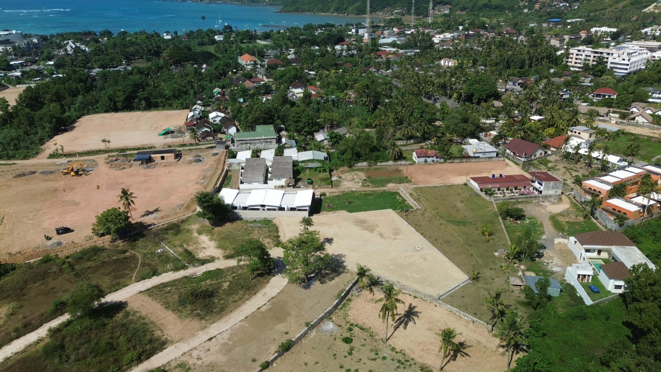 Wide aerial landscape shot showing the plot's proximity to the coastline, access roads, and village area.