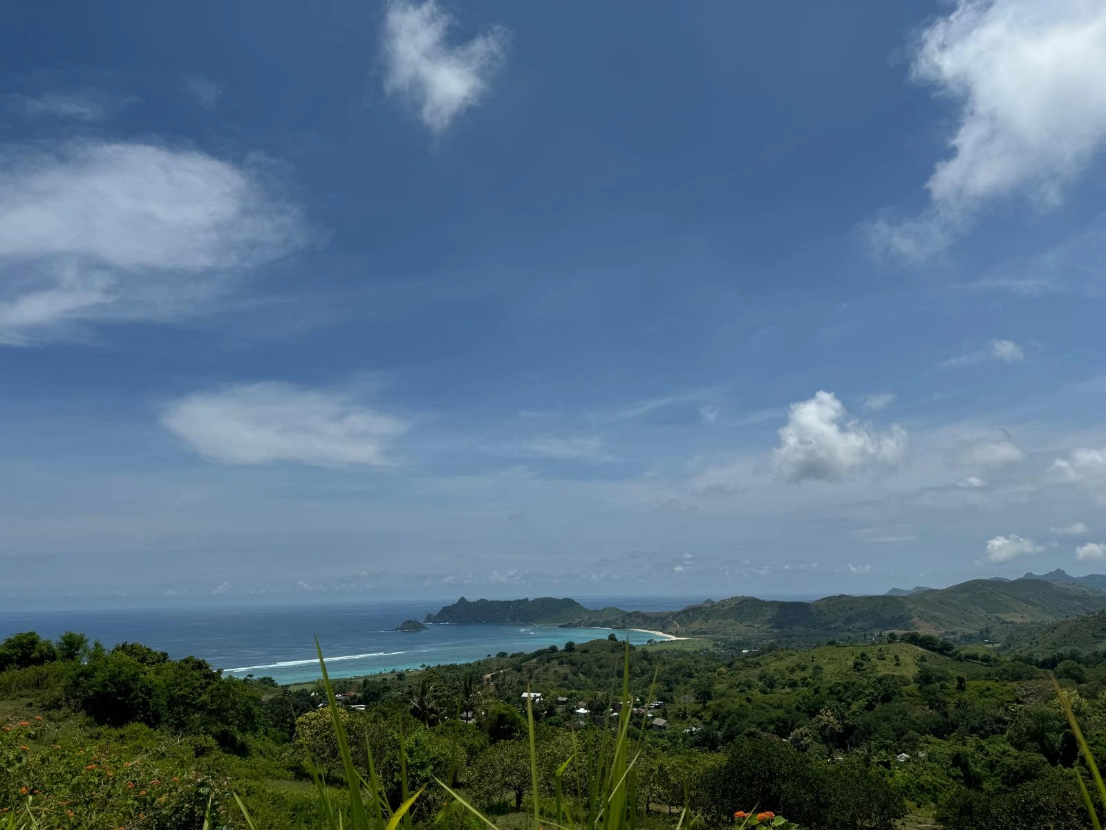 High-angle vantage point showcasing lush green hillsides sloping down toward a clear blue bay and coastal line.