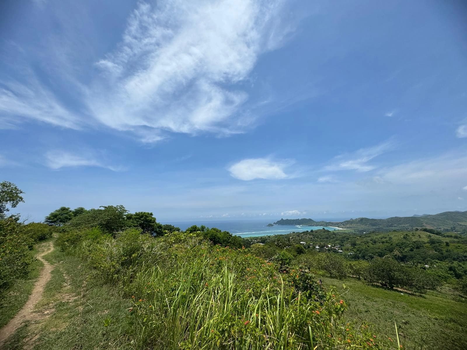 Grassy hilltop perspective overlooking distant ocean waters, featuring a dirt pathway along the left edge.