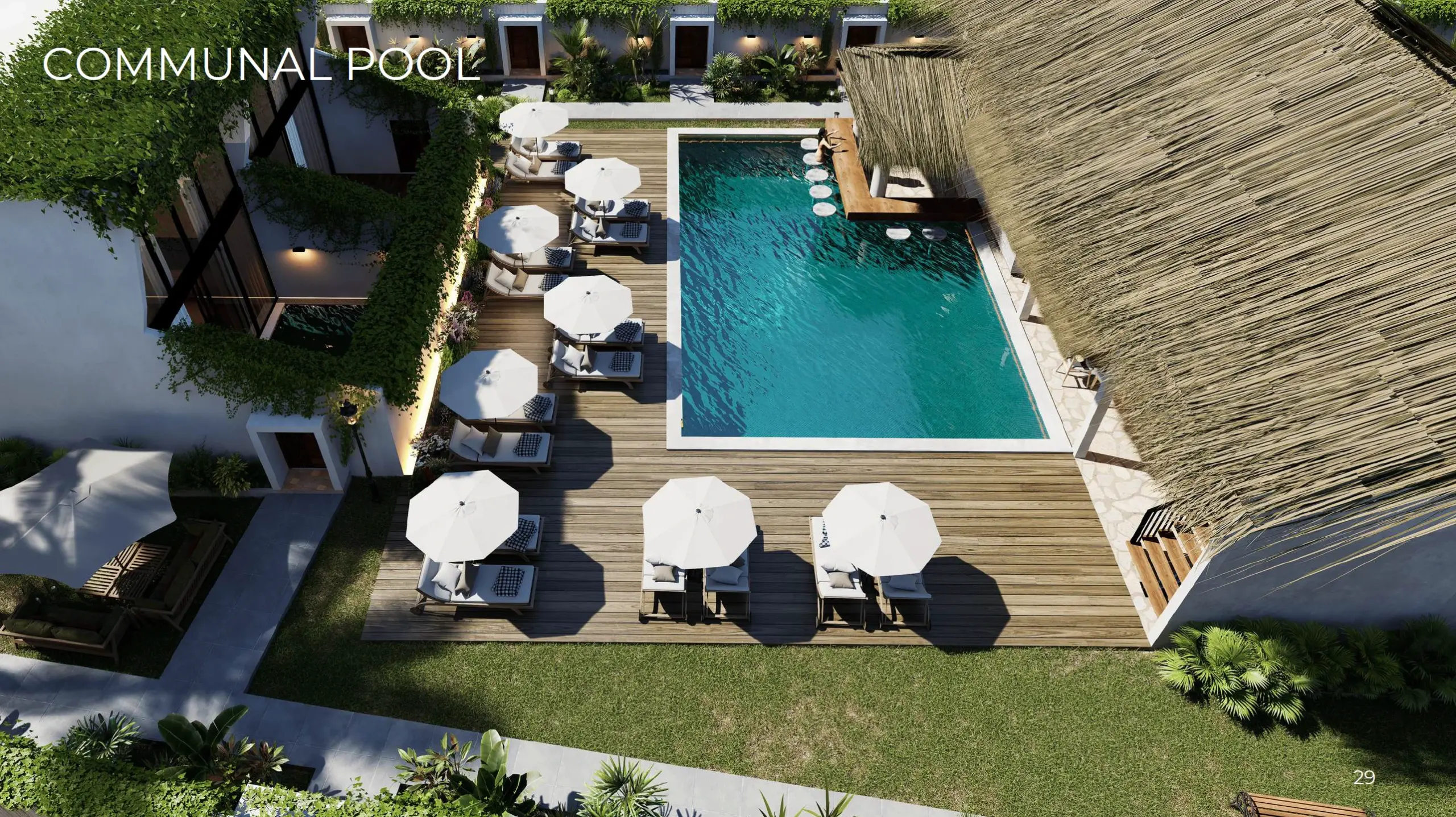 Aerial view of a shared resort pool surrounded by a wooden deck with sun umbrellas, loungers, and tropical landscaping.