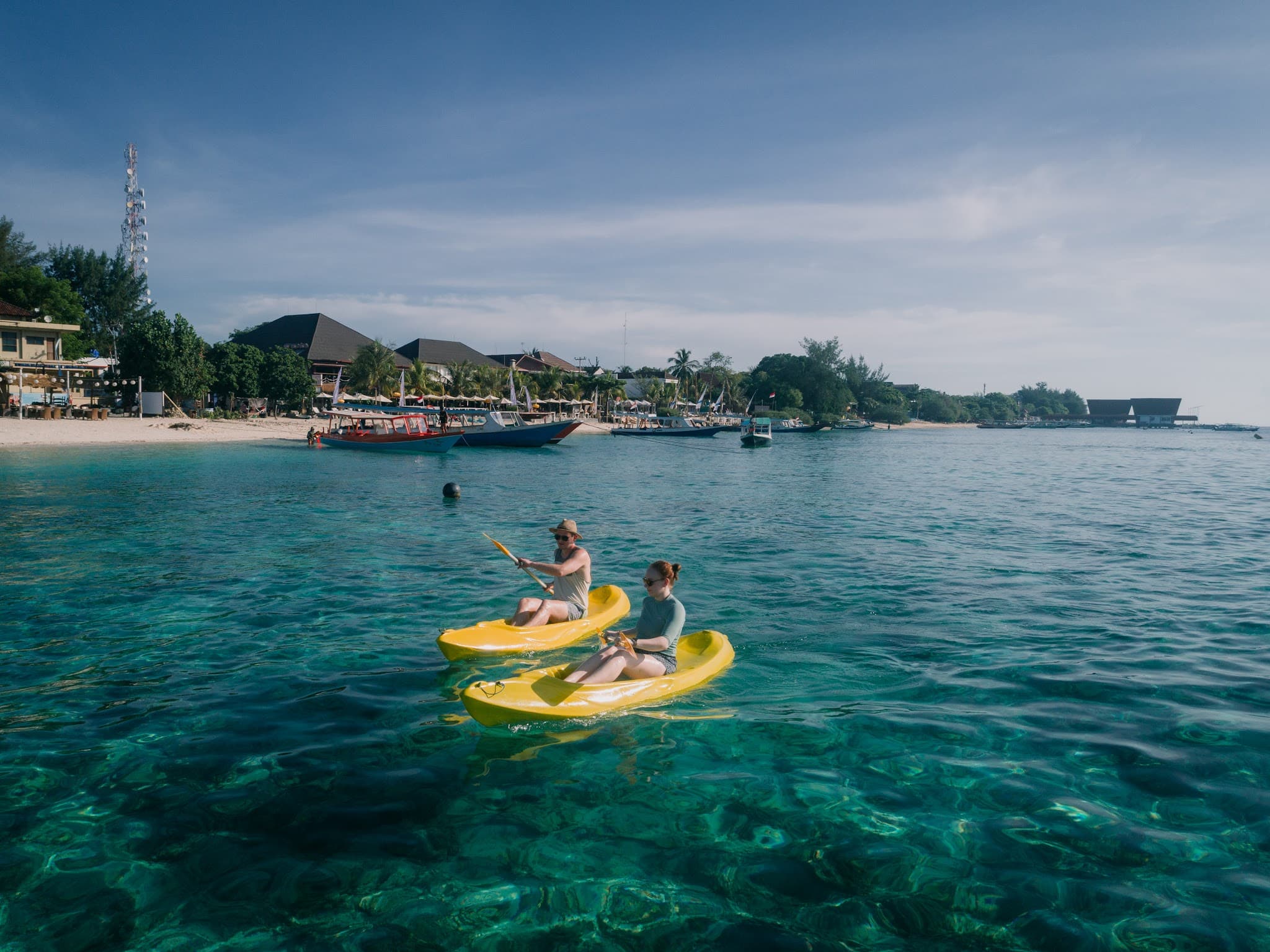 Two people kayaking in clear turquoise water near a beach.