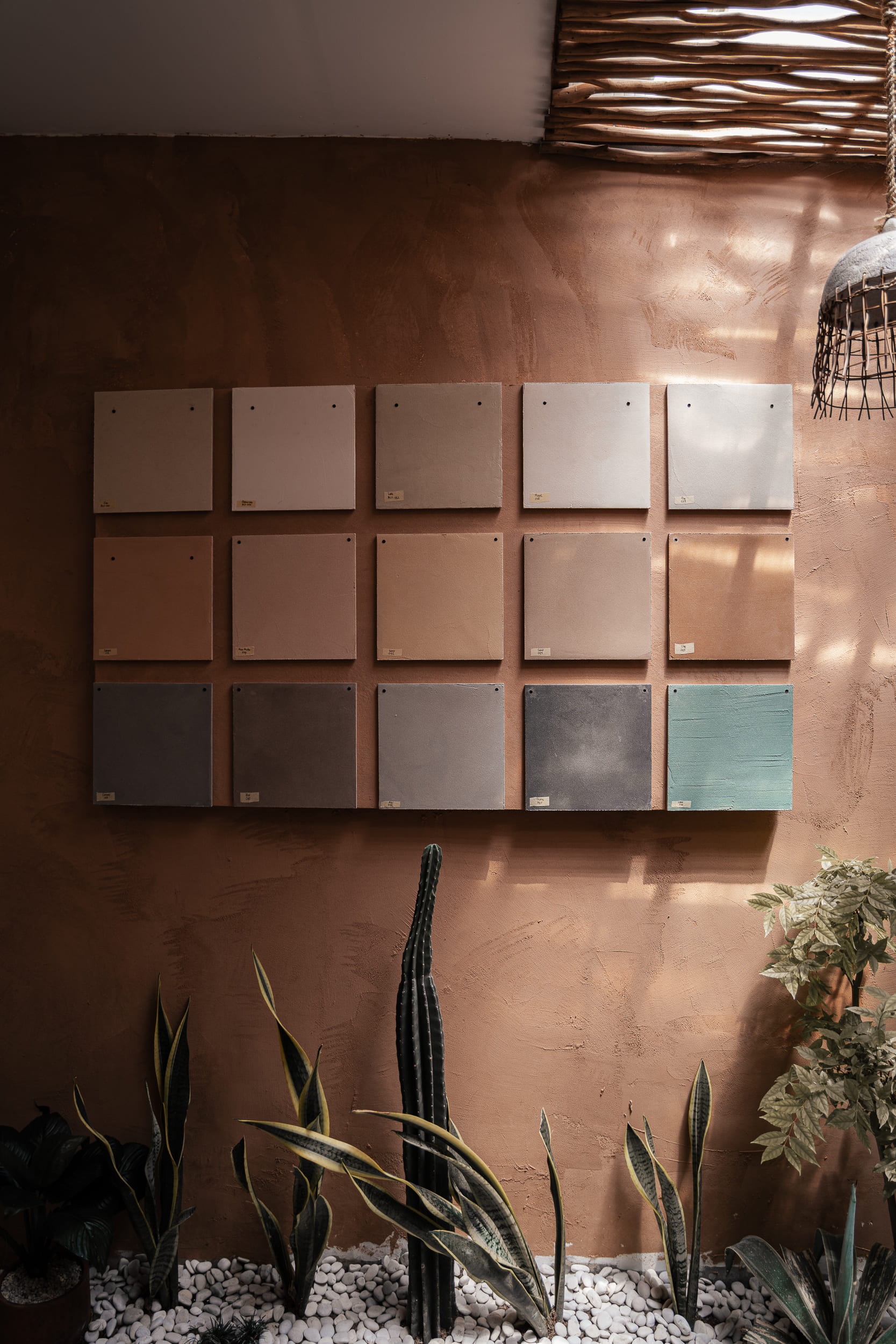 Grid of material finish swatches on a terracotta wall above indoor plants.