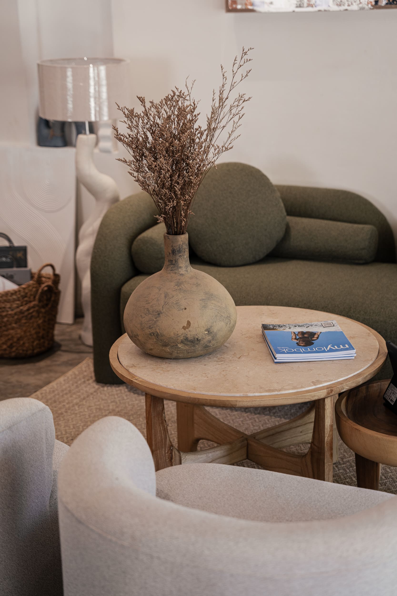 Earthy vase with dried grasses on a marble coffee table and an olive-green sofa.