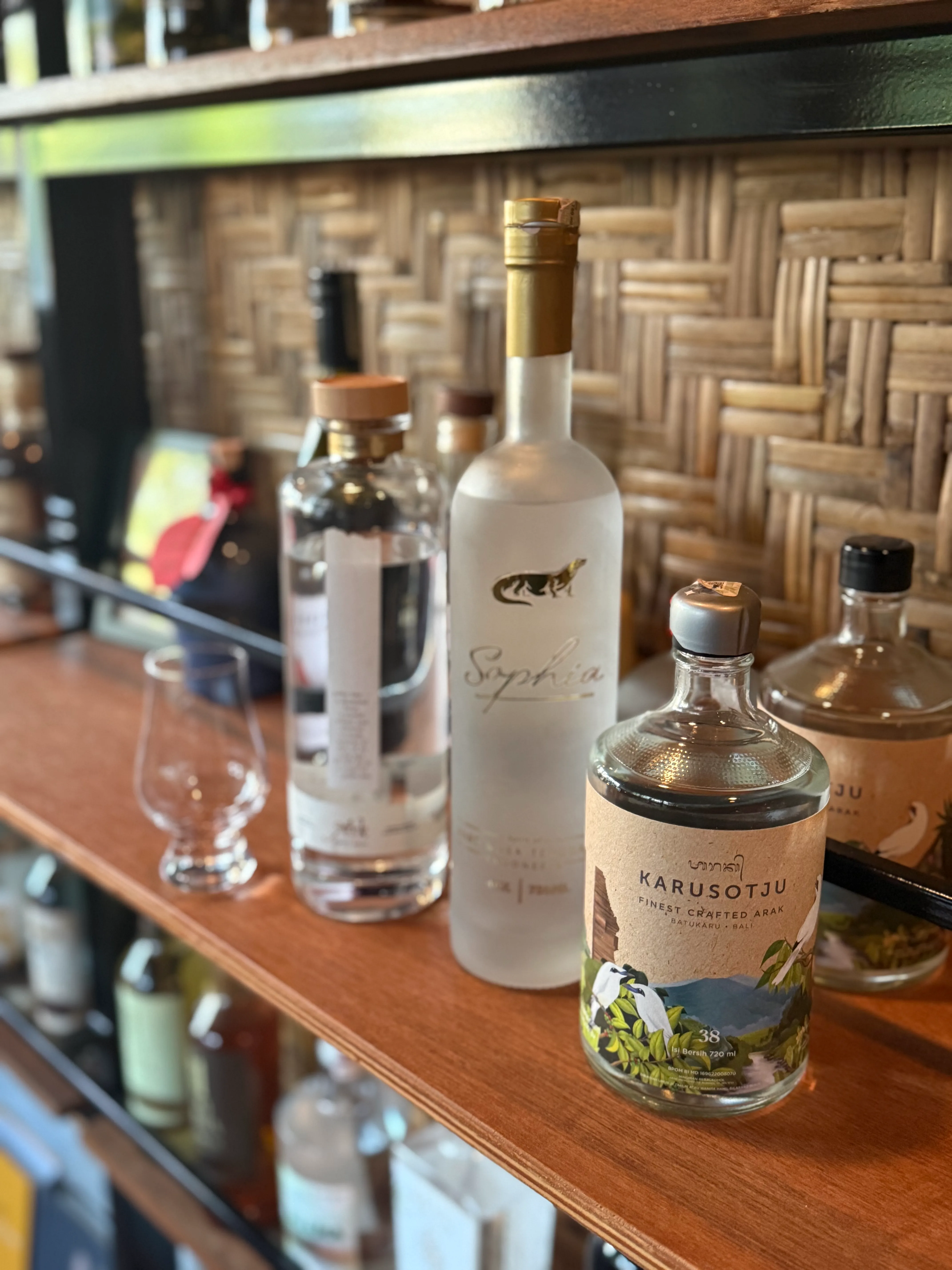 Close-up of craft liquor bottles—including Karusotju Arak and Sophia—on a wooden bar shelf.