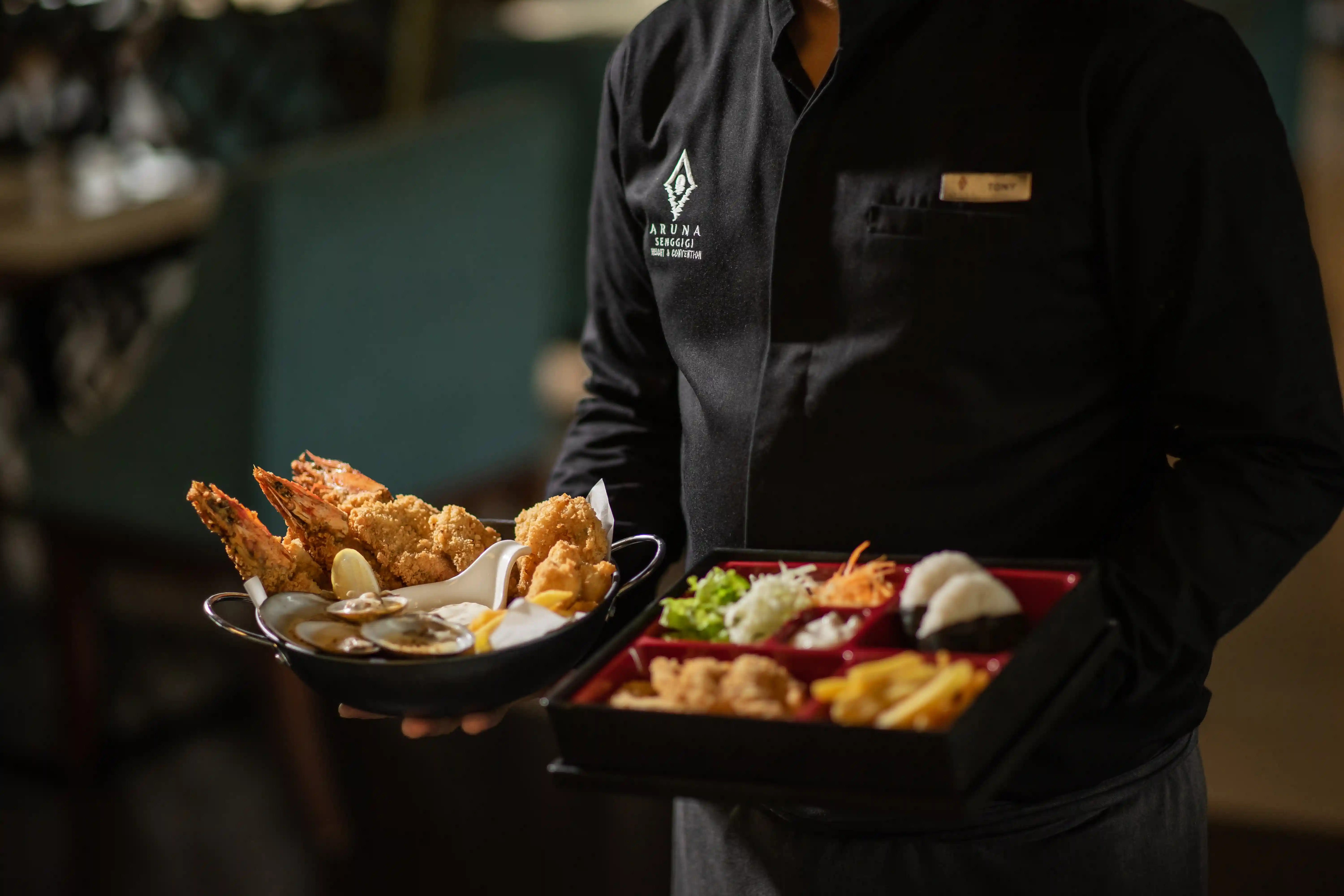 Waiter serving a platter of deep-fried seafood and a Japanese bento box.