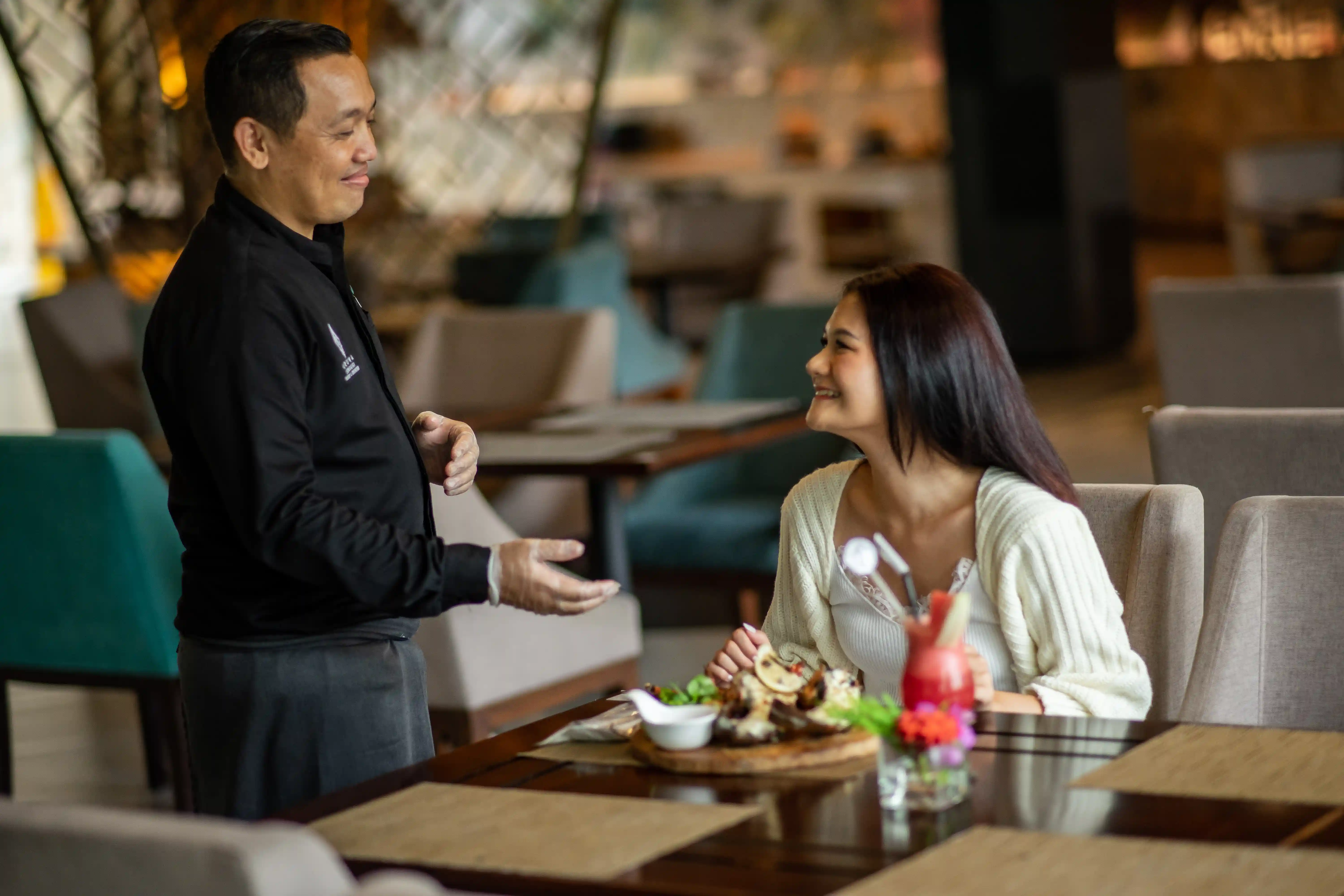 Smiling waiter taking an order from a female guest seated at an upscale restaurant table.