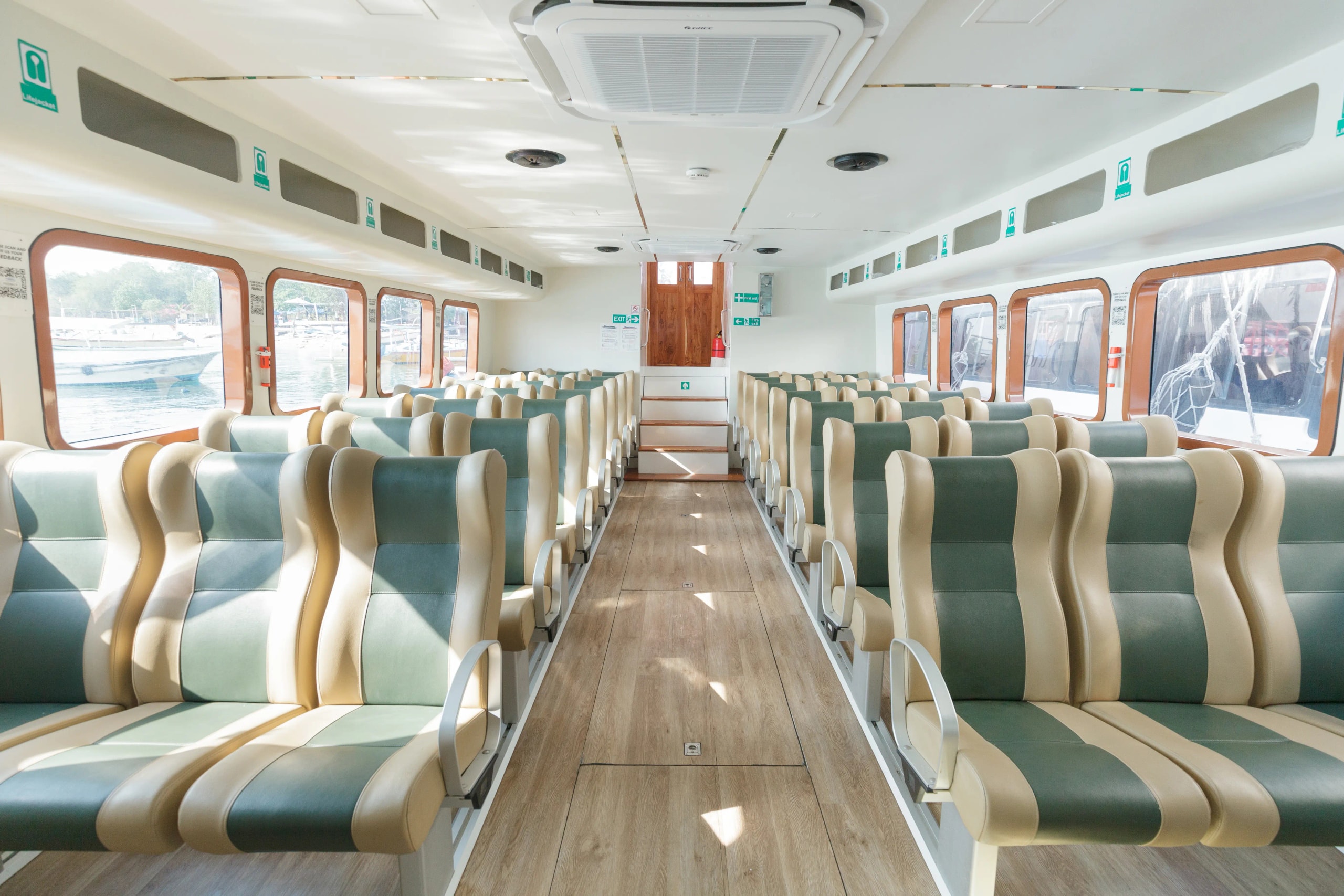 Interior view of a fast boat passenger cabin featuring rows of green and beige leather seats, large windows, and central air conditioning.