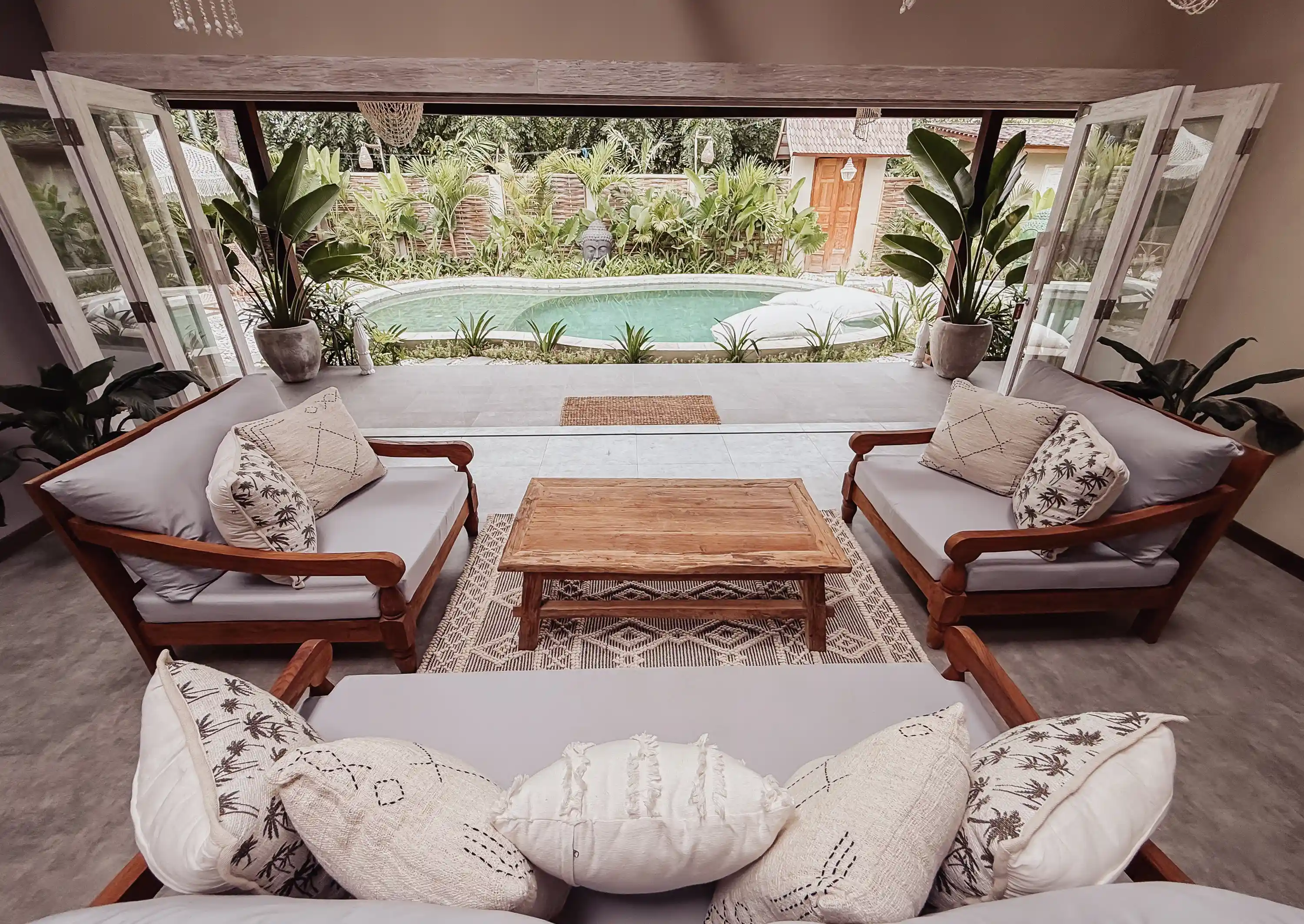 Salon lumineux aux portes vitrées entièrement ouvertes offrant une vue directe sur la piscine et le jardin.