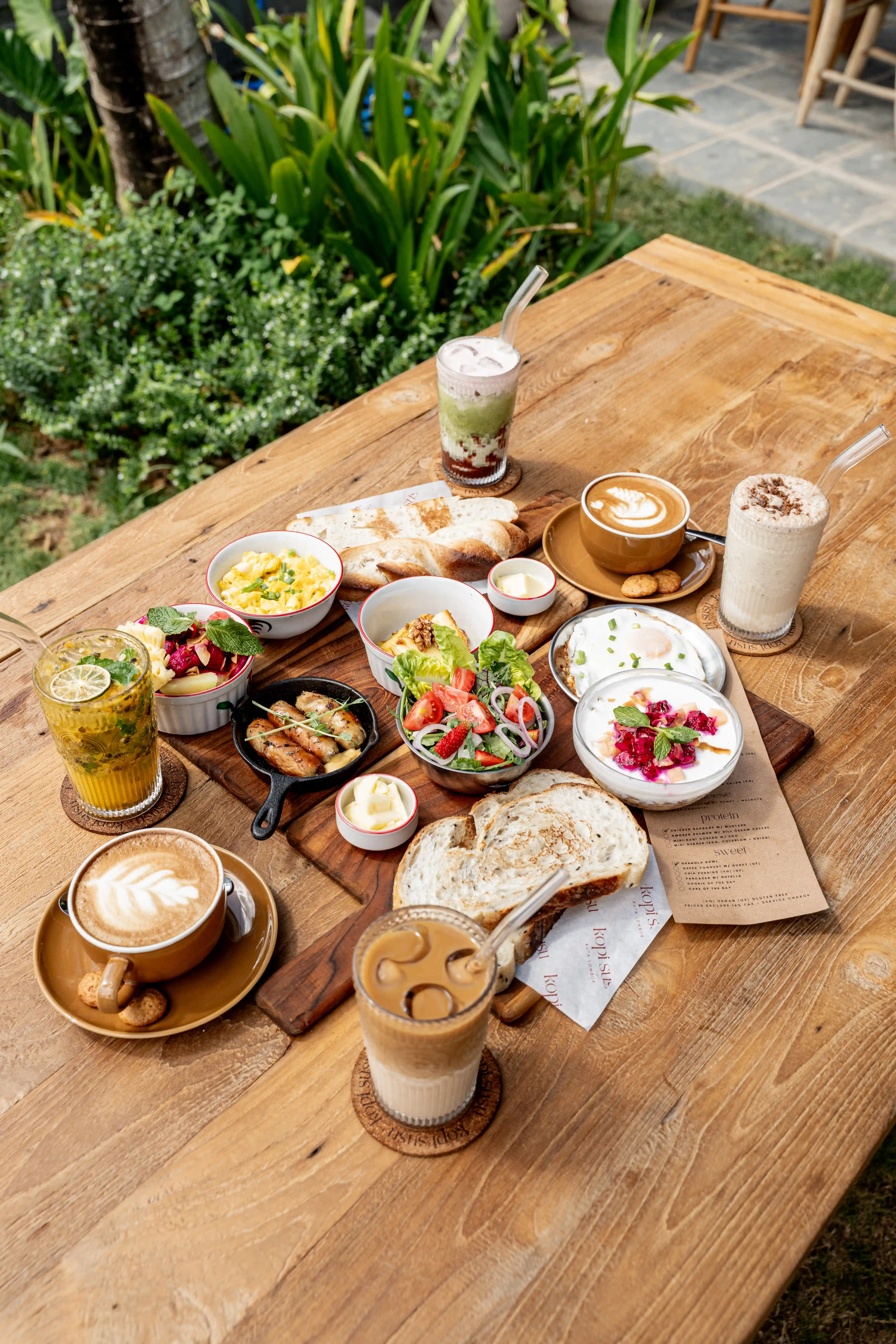Overhead view of a colorful breakfast spread with bread, eggs, salad, yogurt, pastries, and coffee.
