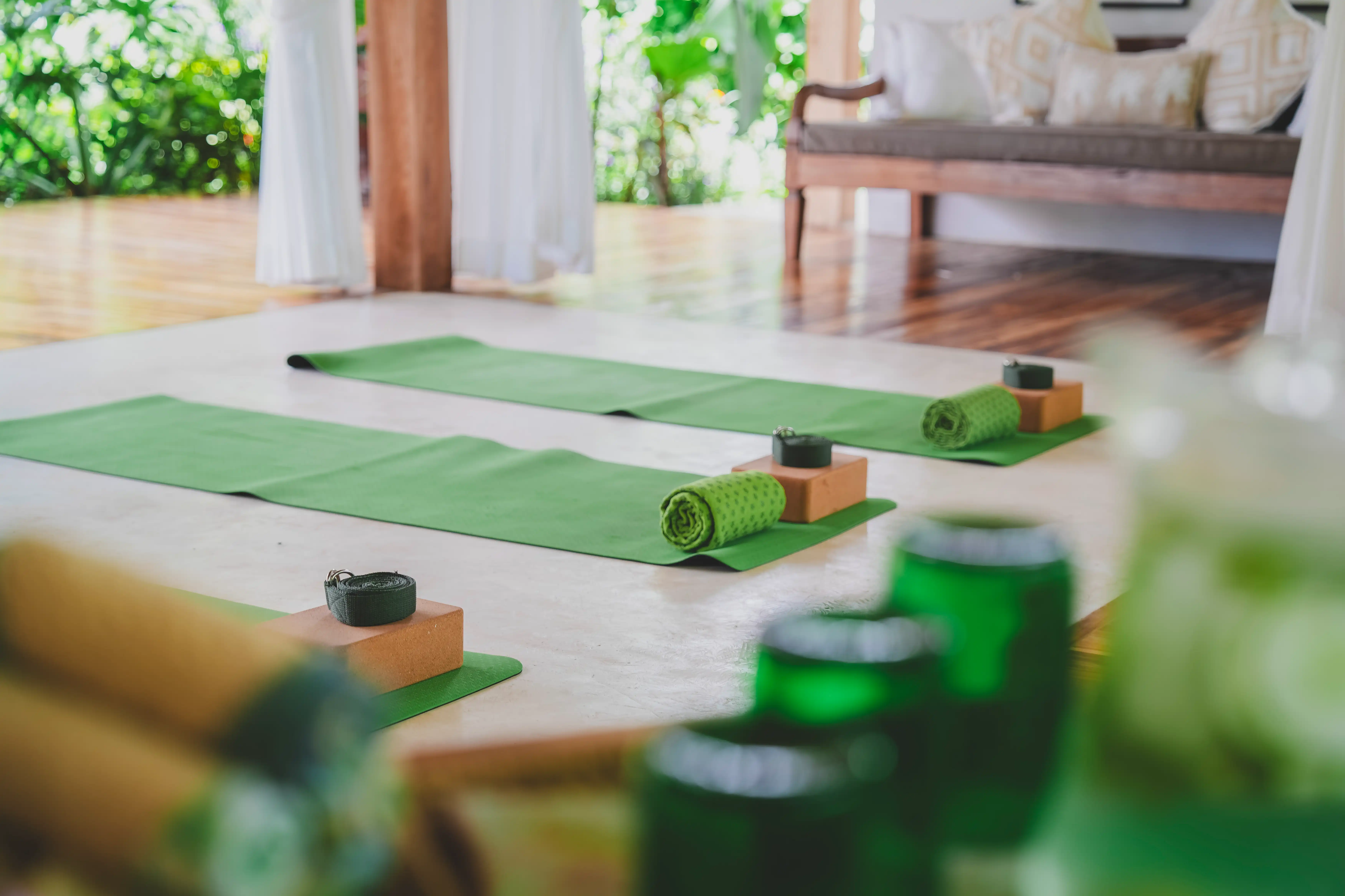 Green yoga mats set up with rolled towels and yoga blocks in an open-air pavilion.