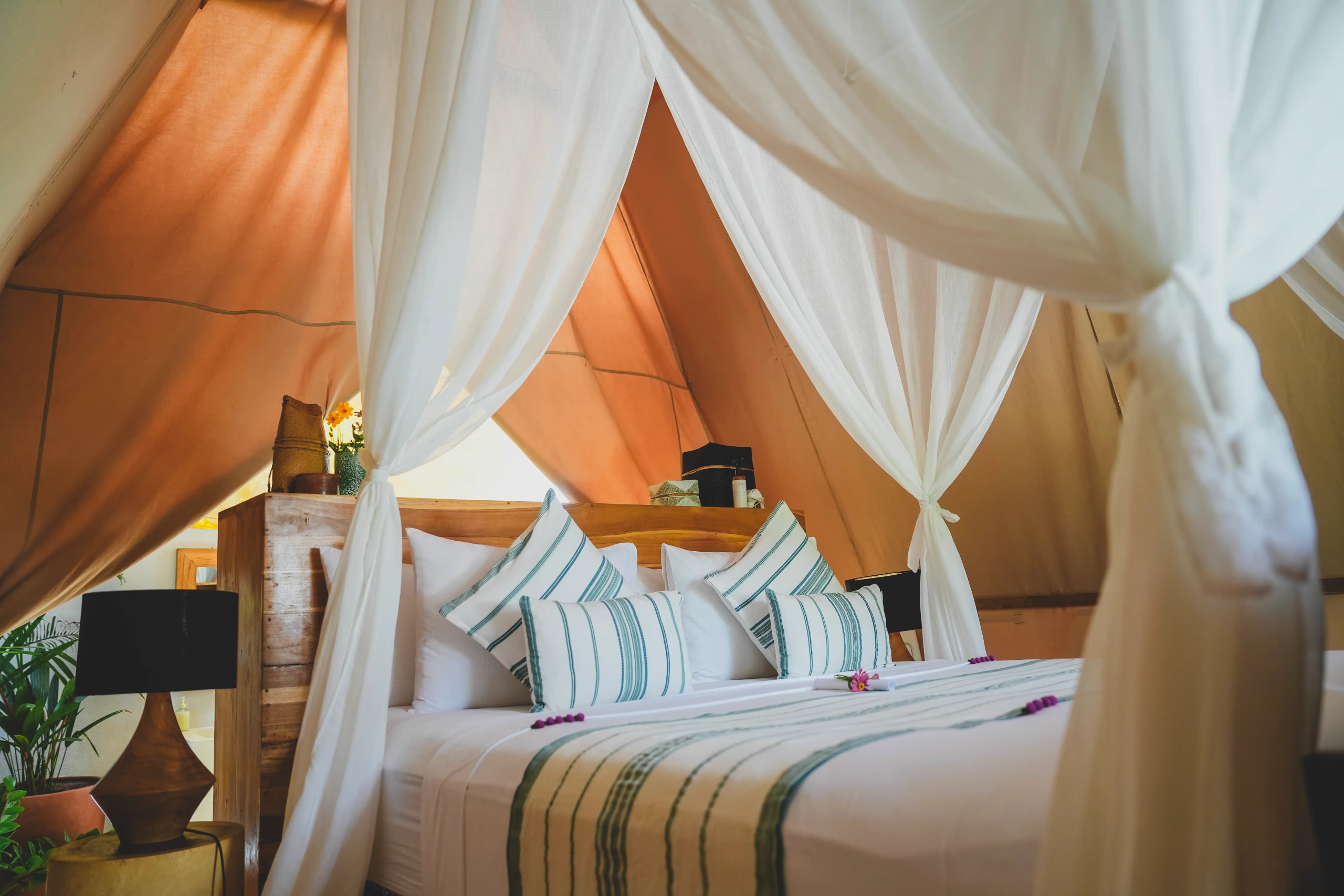 Interior of a glamping tent featuring a large bed draped with white mosquito netting and decorative pillows.