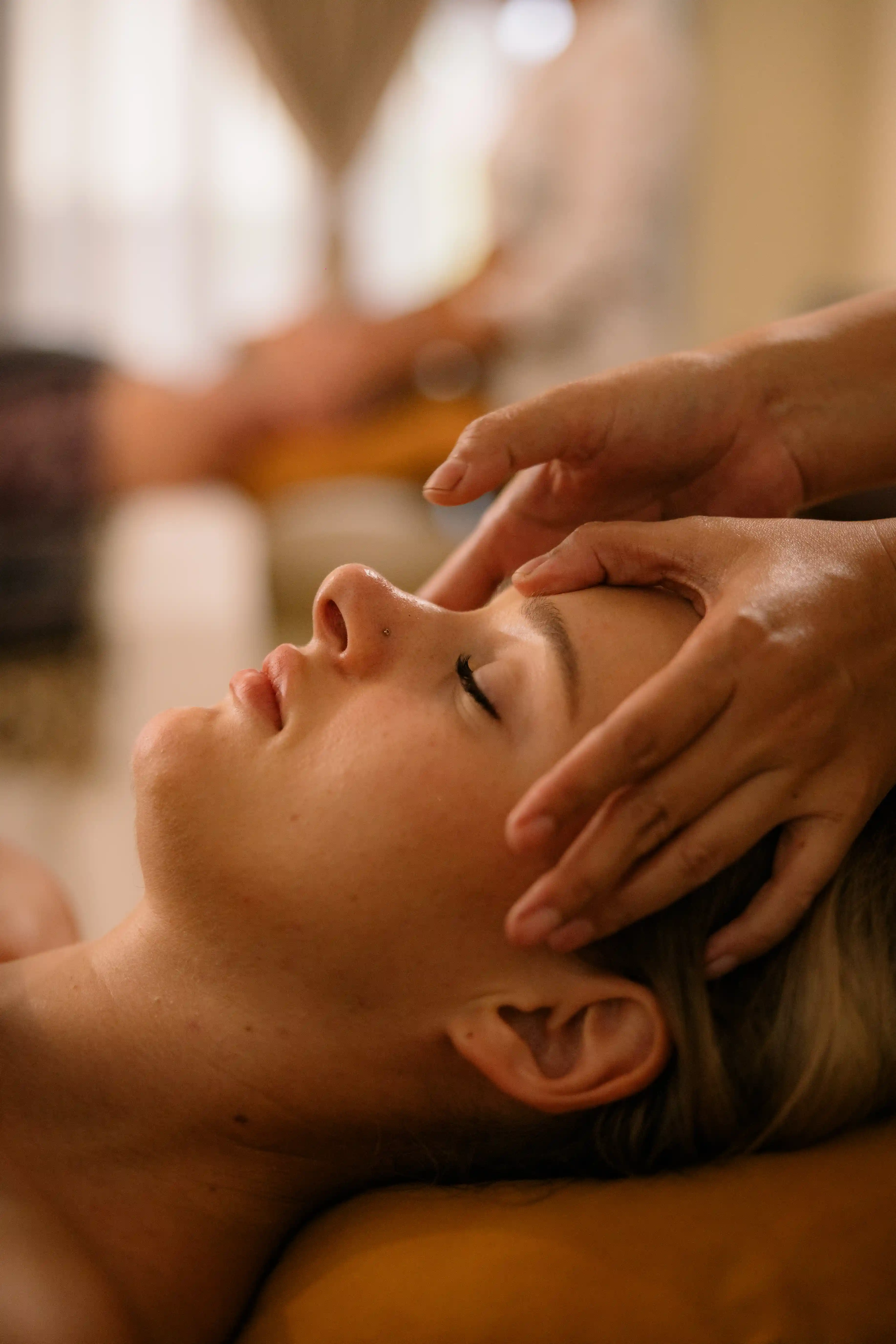 Close-up profile view of a woman receiving a gentle forehead massage during a spa treatment.