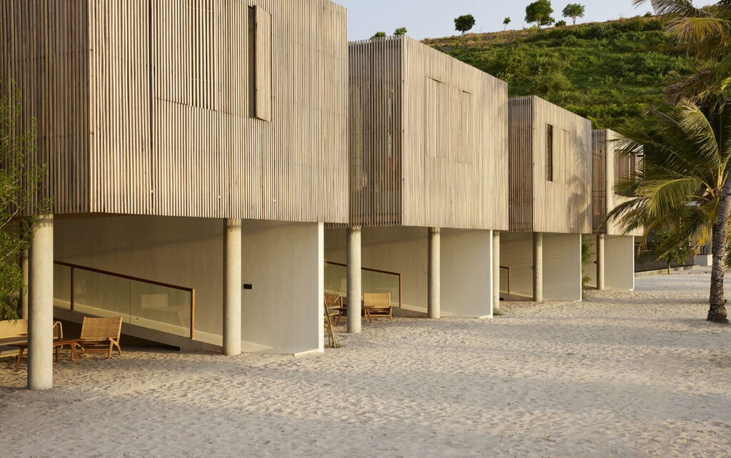 Modern wooden stilt villas set directly on a sandy beach.