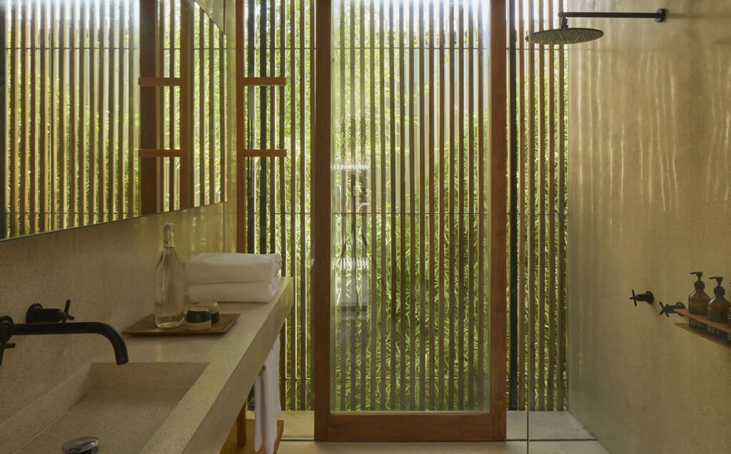 Minimalist bathroom featuring a stone trough sink, overhead shower, and wooden slats.