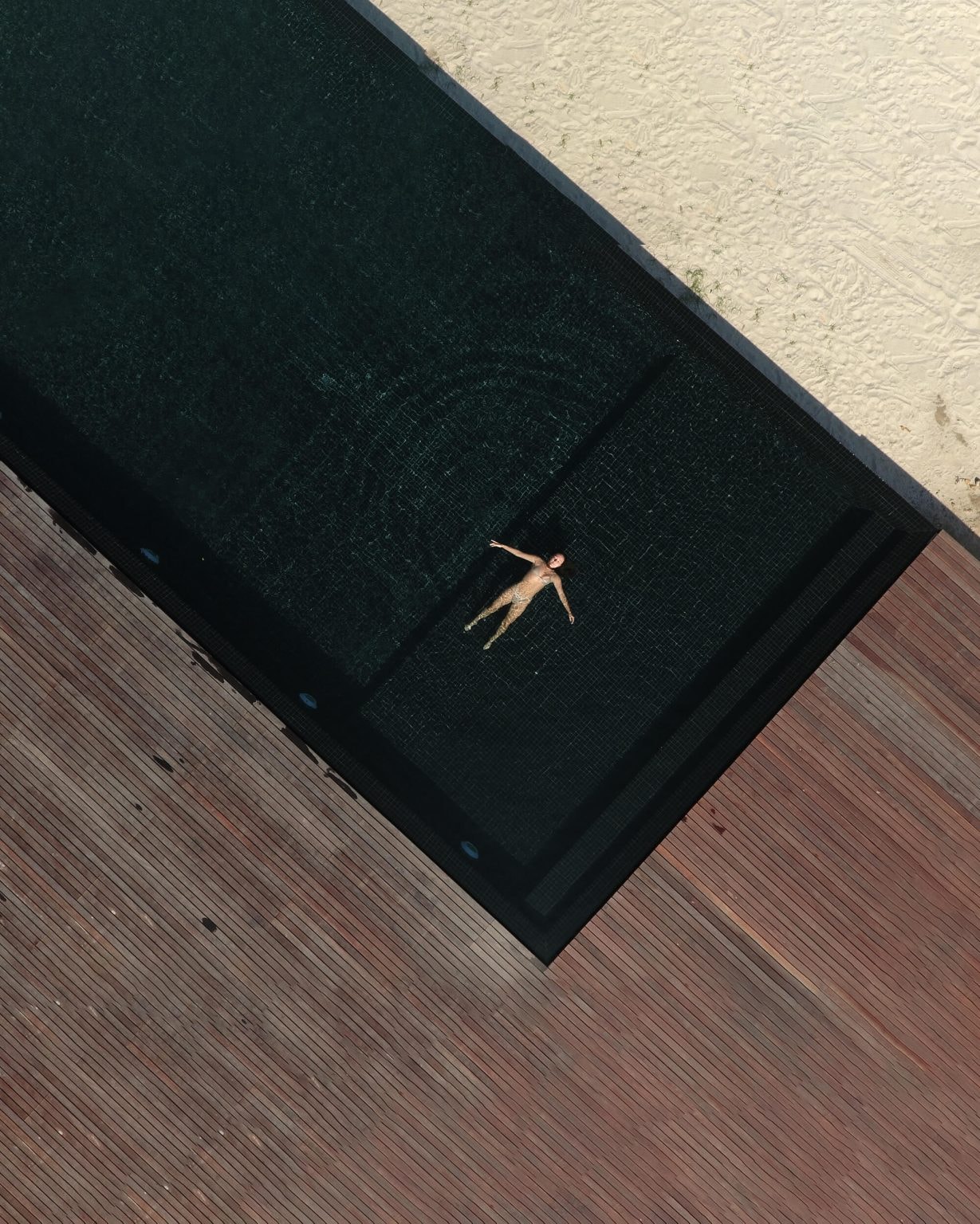 Overhead aerial shot of a person floating in a dark infinity pool next to the beach.
