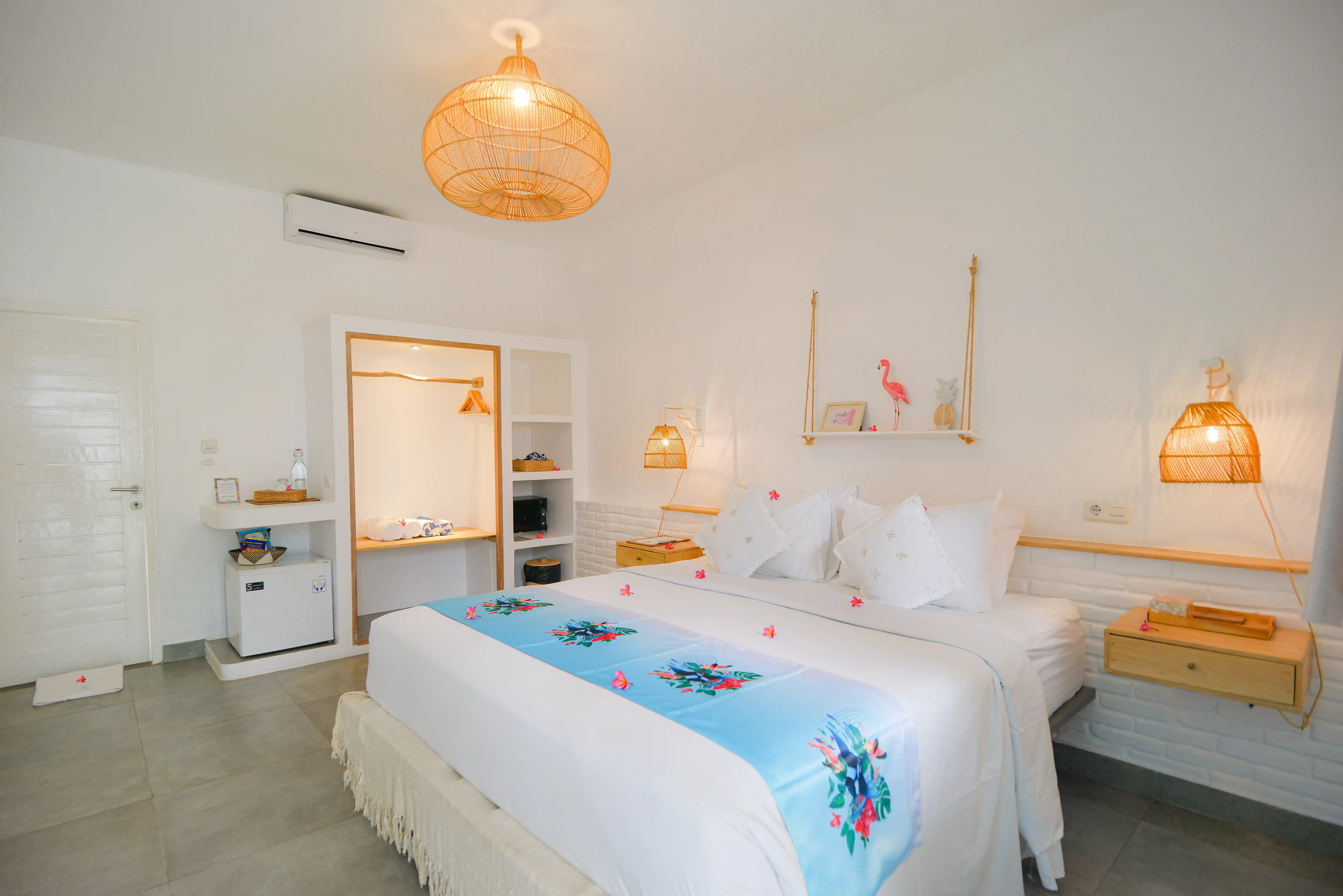 Chambre lumineuse avec grand lit double, décorations tropicales, suspensions en rotin et chemin de lit bleu.