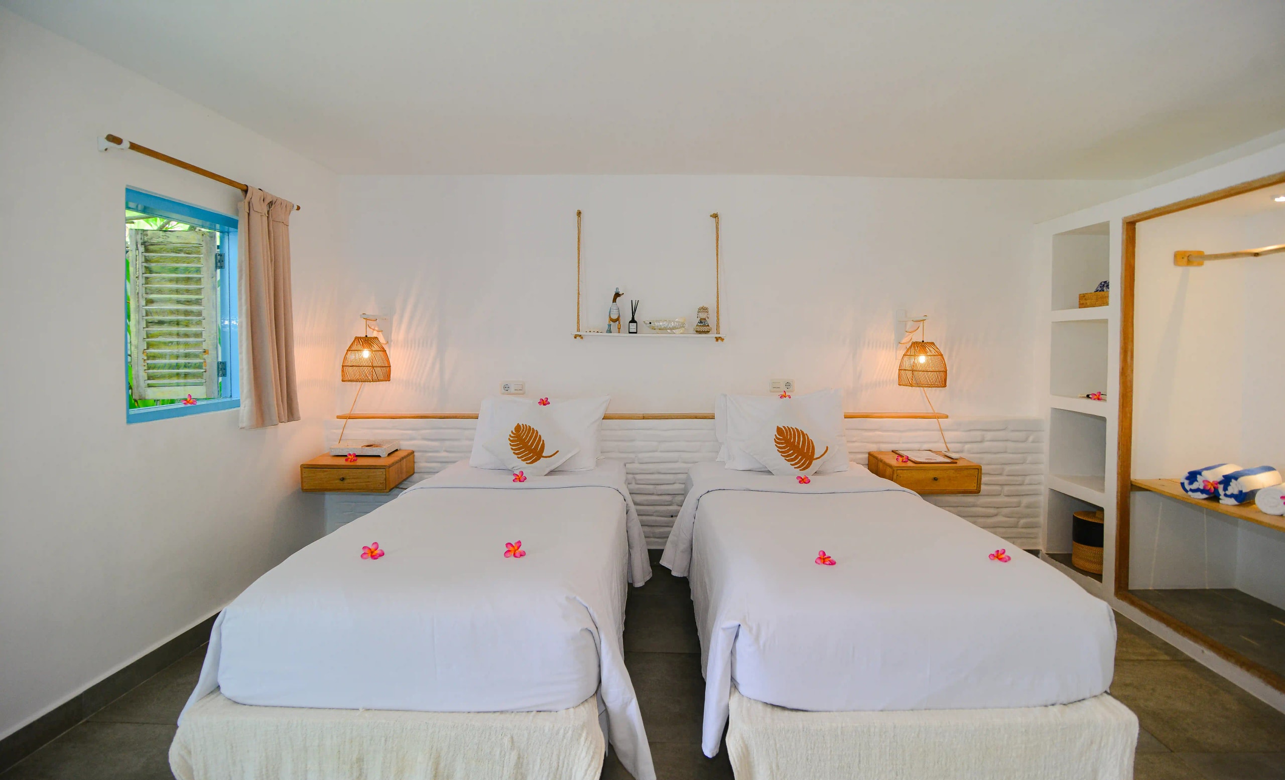 Chambre d'hôtel moderne équipée de deux lits simples décorés de fleurs et de lampes de chevet en tissage.
