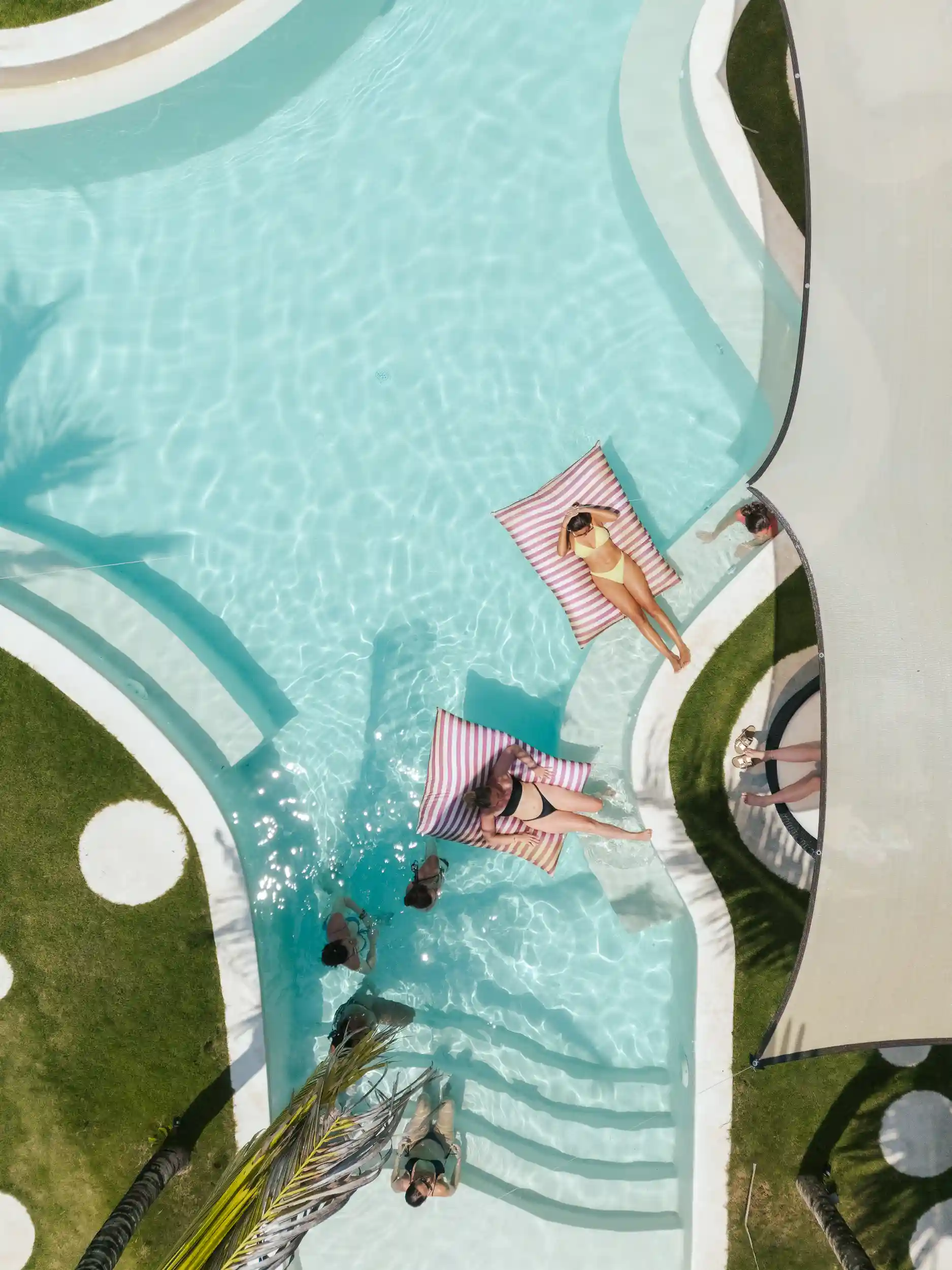 Vue du dessus de clients se détendant dans une piscine turquoise sur des matelas flottants rayés.