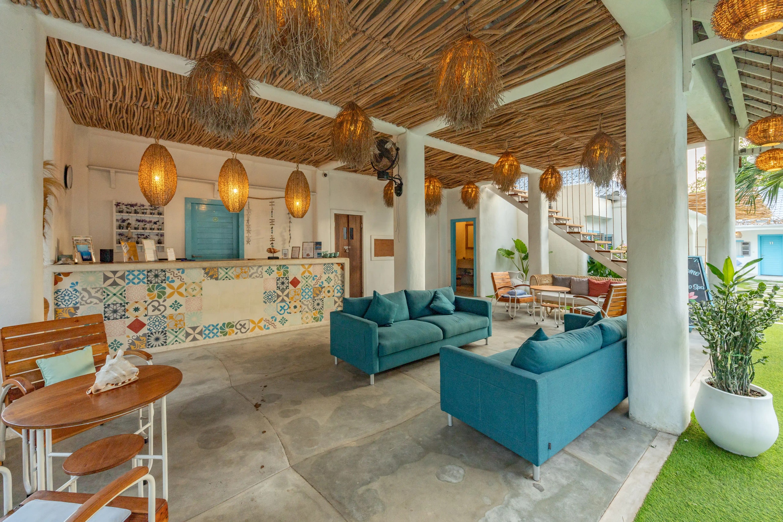 Lobby ouvert de l'hôtel avec canapés bleus, plafond en bois rustique et comptoir en carrelage coloré.