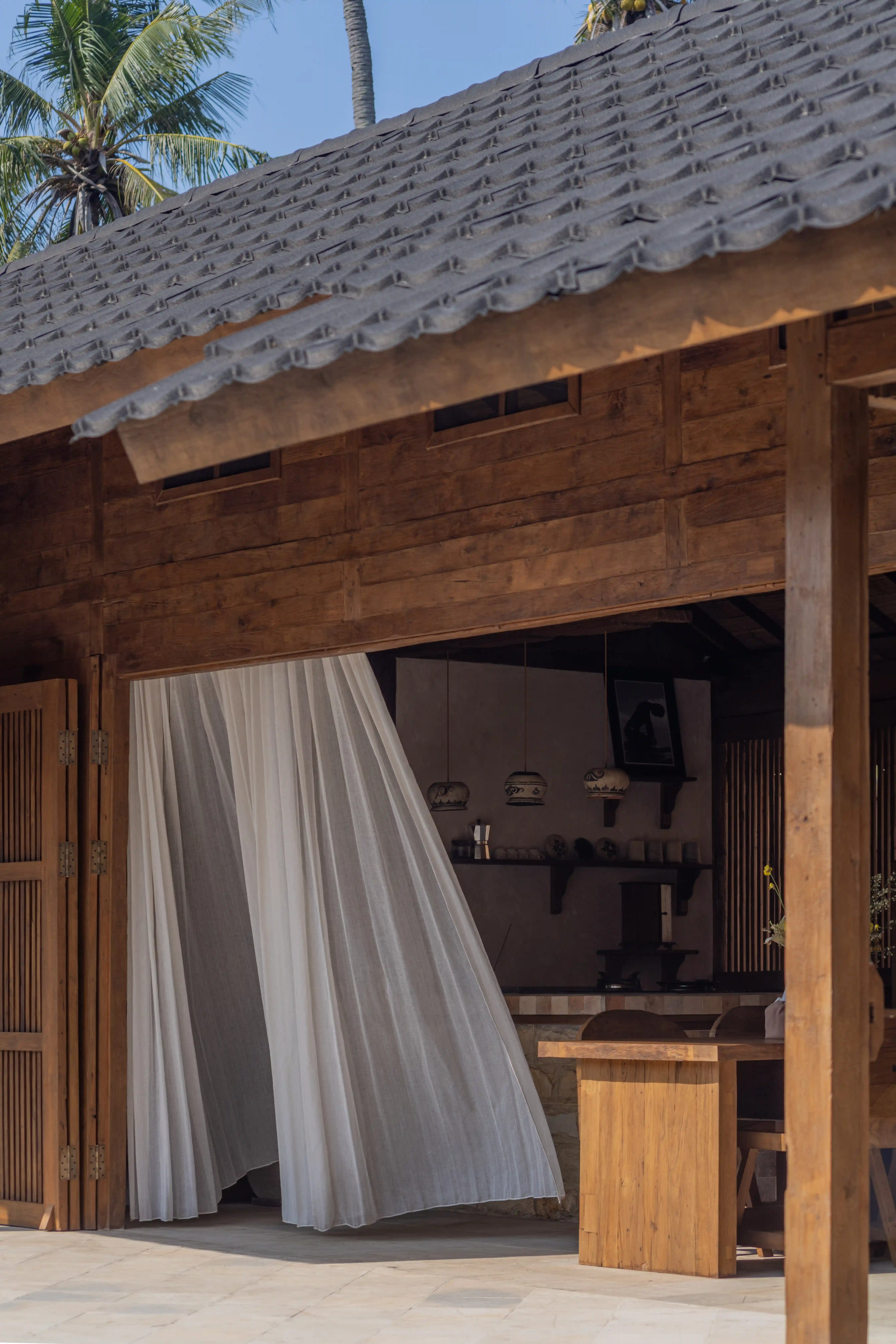 Exterior view of a wooden villa with a tiled roof and sheer white curtains blowing in the breeze.