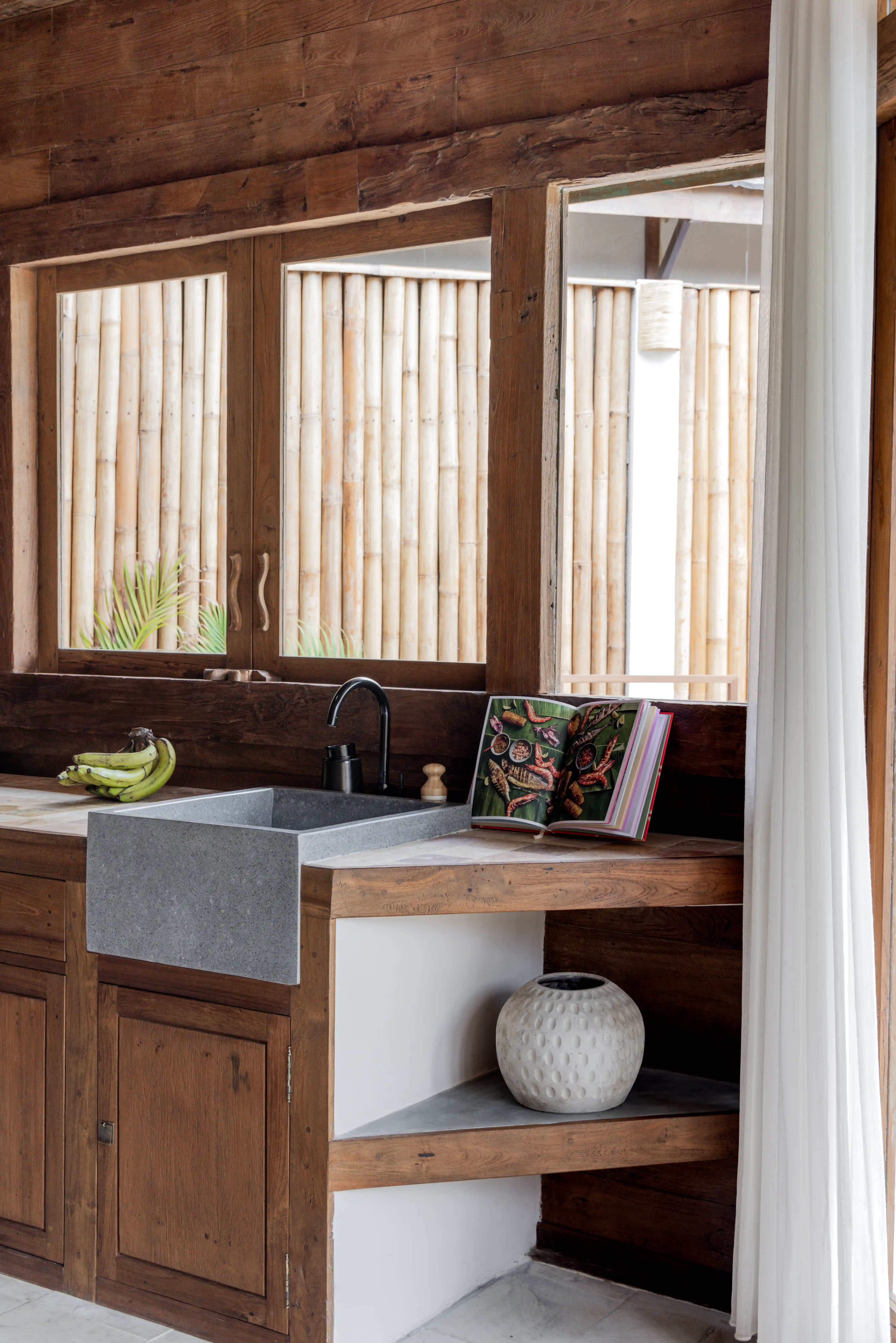 Kitchen counter with a stone sink, wooden cabinetry, a book on display, and a window framed by bamboo fencing.