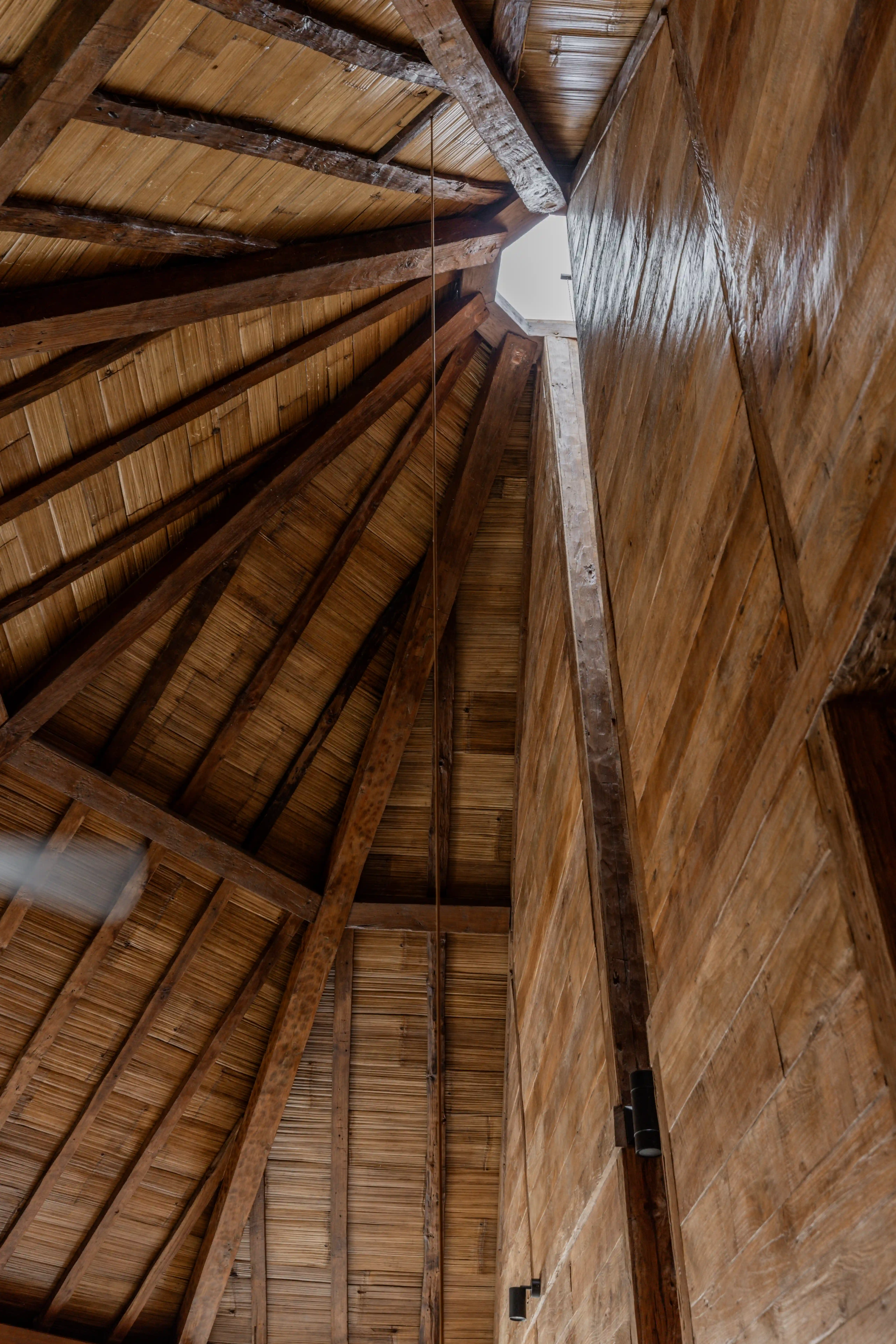 Upward interior view of a high, vaulted roof crafted from exposed wooden beams and woven bamboo.