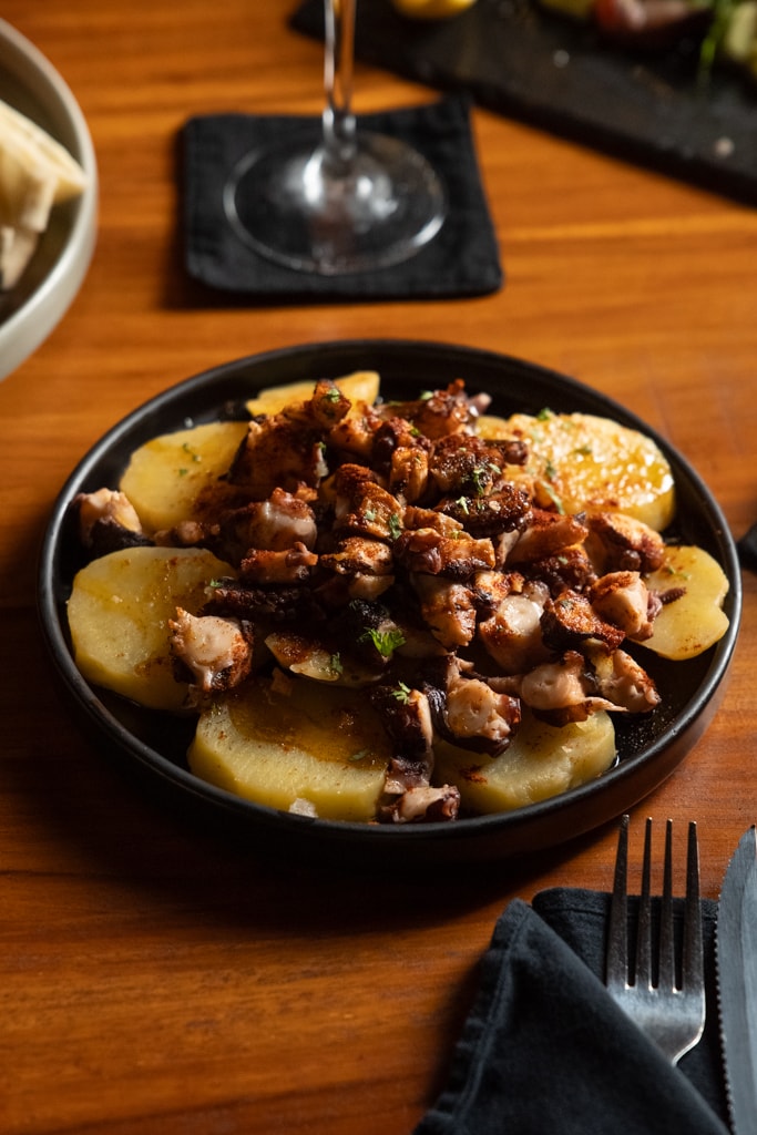 Seared octopus slices over boiled potatoes served on a black plate.