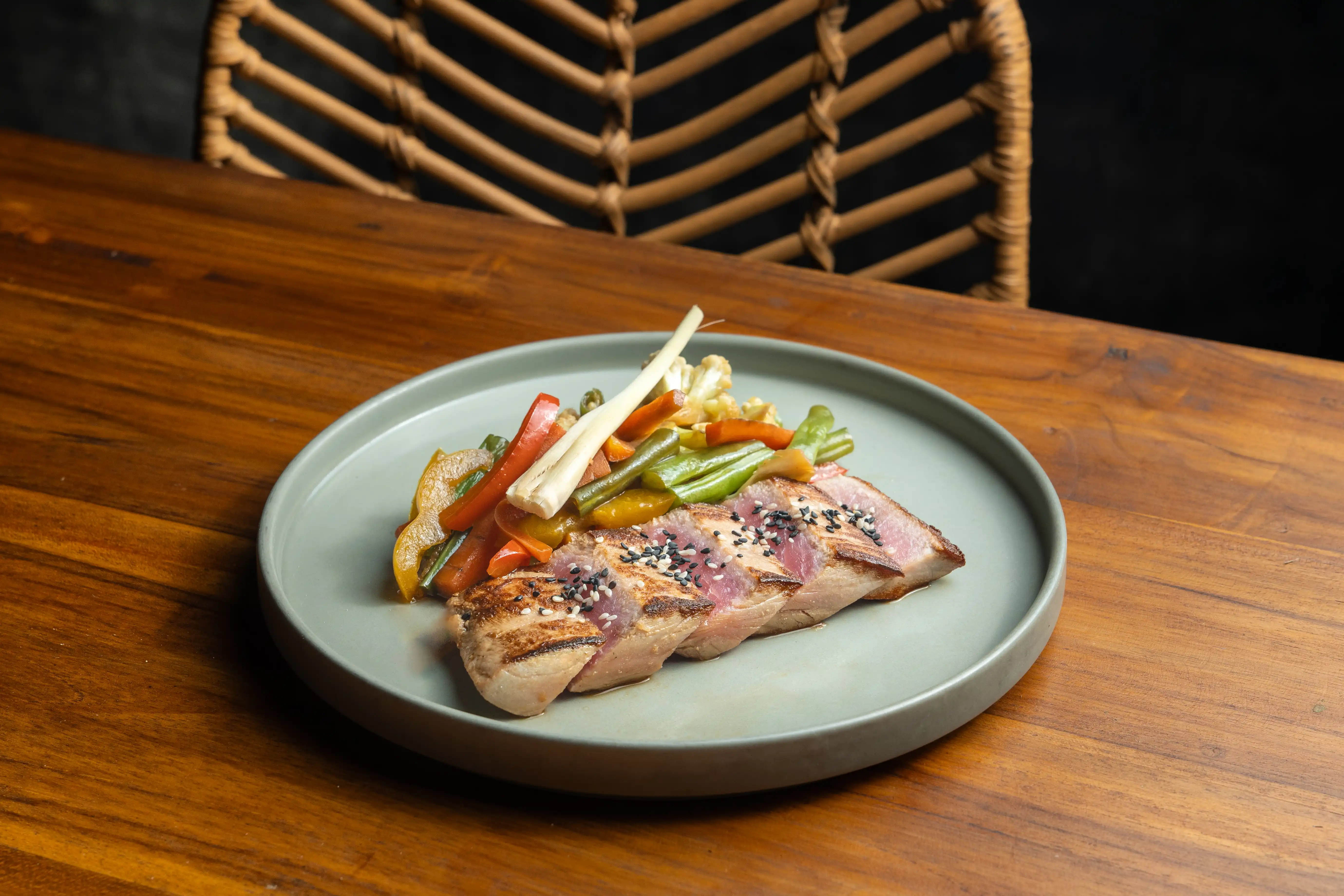 Seared tuna steak slices with sesame seeds and sauteed vegetables on a grey plate.