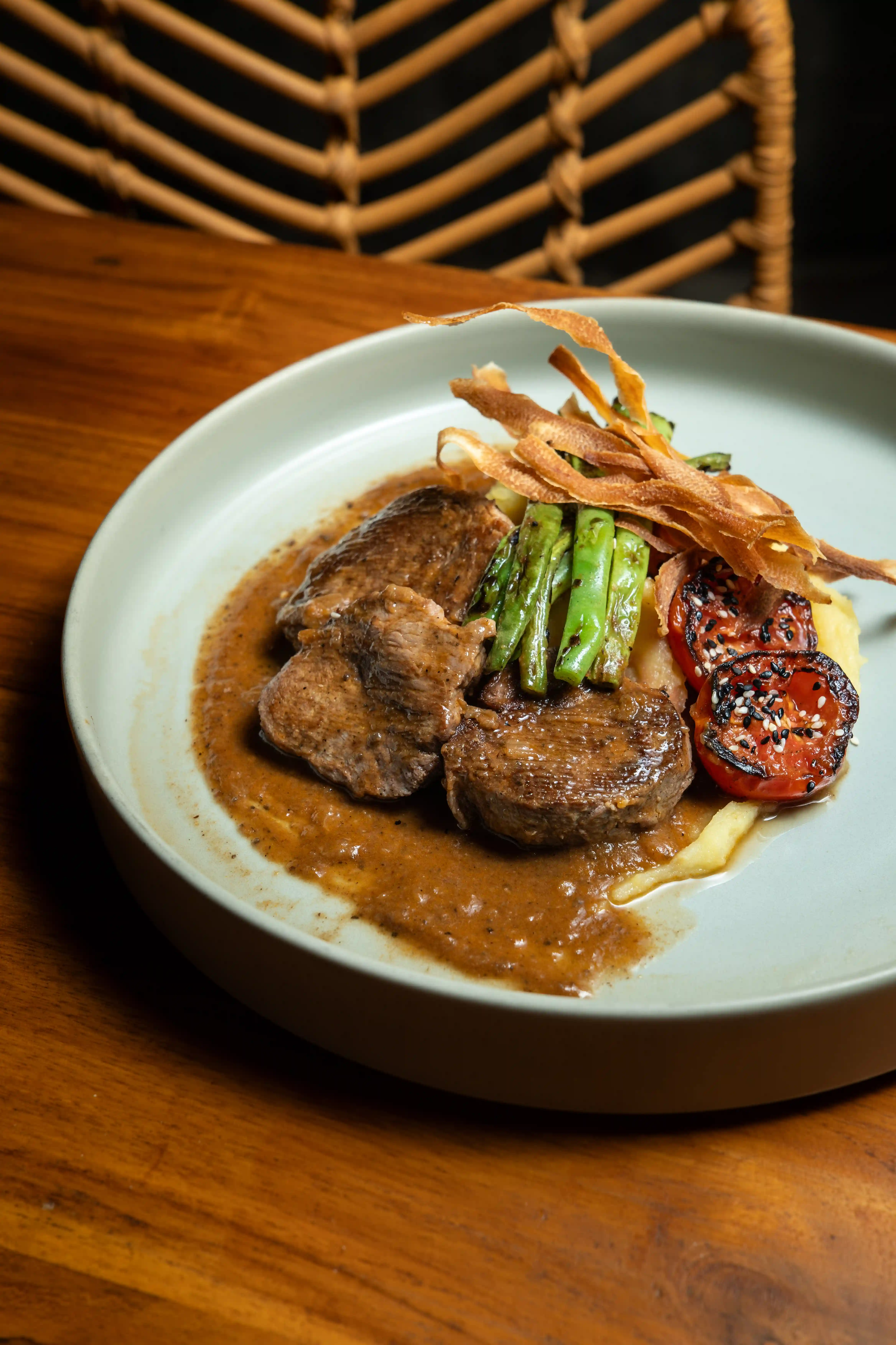 Tenderloin steak with gravy sauce, grilled tomatoes, and green beans on a grey plate.