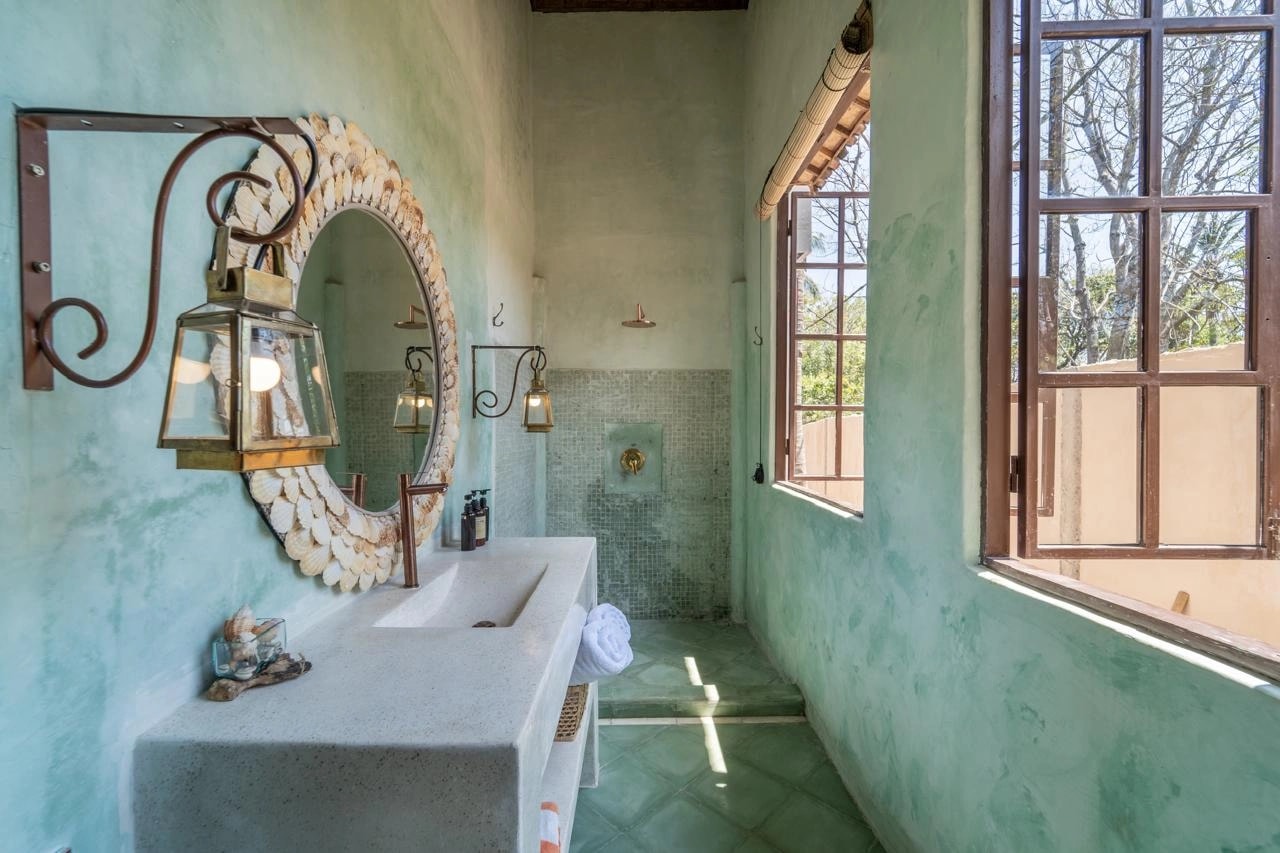 Salle de bain verte avec miroir en coquillages et meuble vasque en béton.