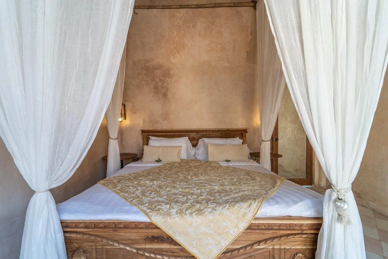 Lit en bois sculpté avec baldaquin blanc dans une chambre au style rustique.