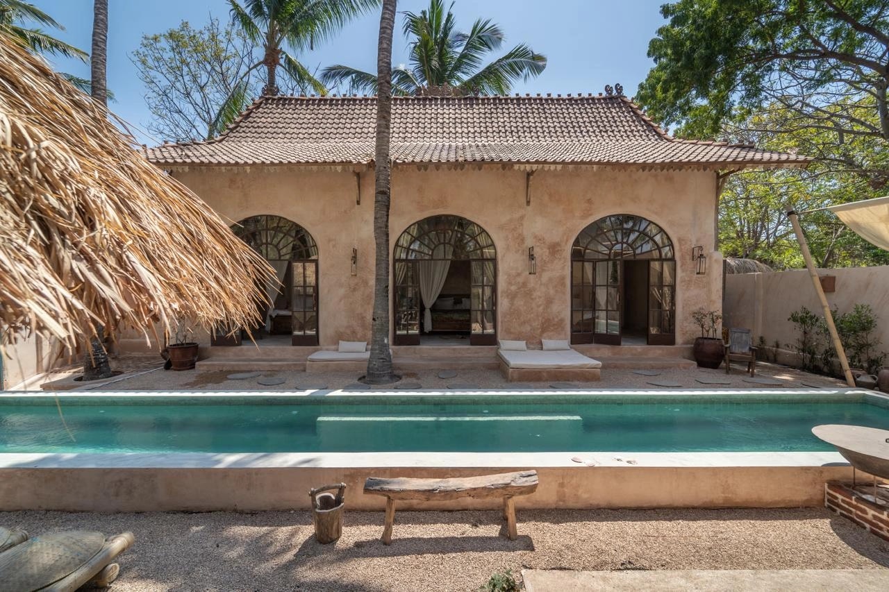 Façade d'une villa en pierre avec piscine tout le long et grandes portes voûtées.