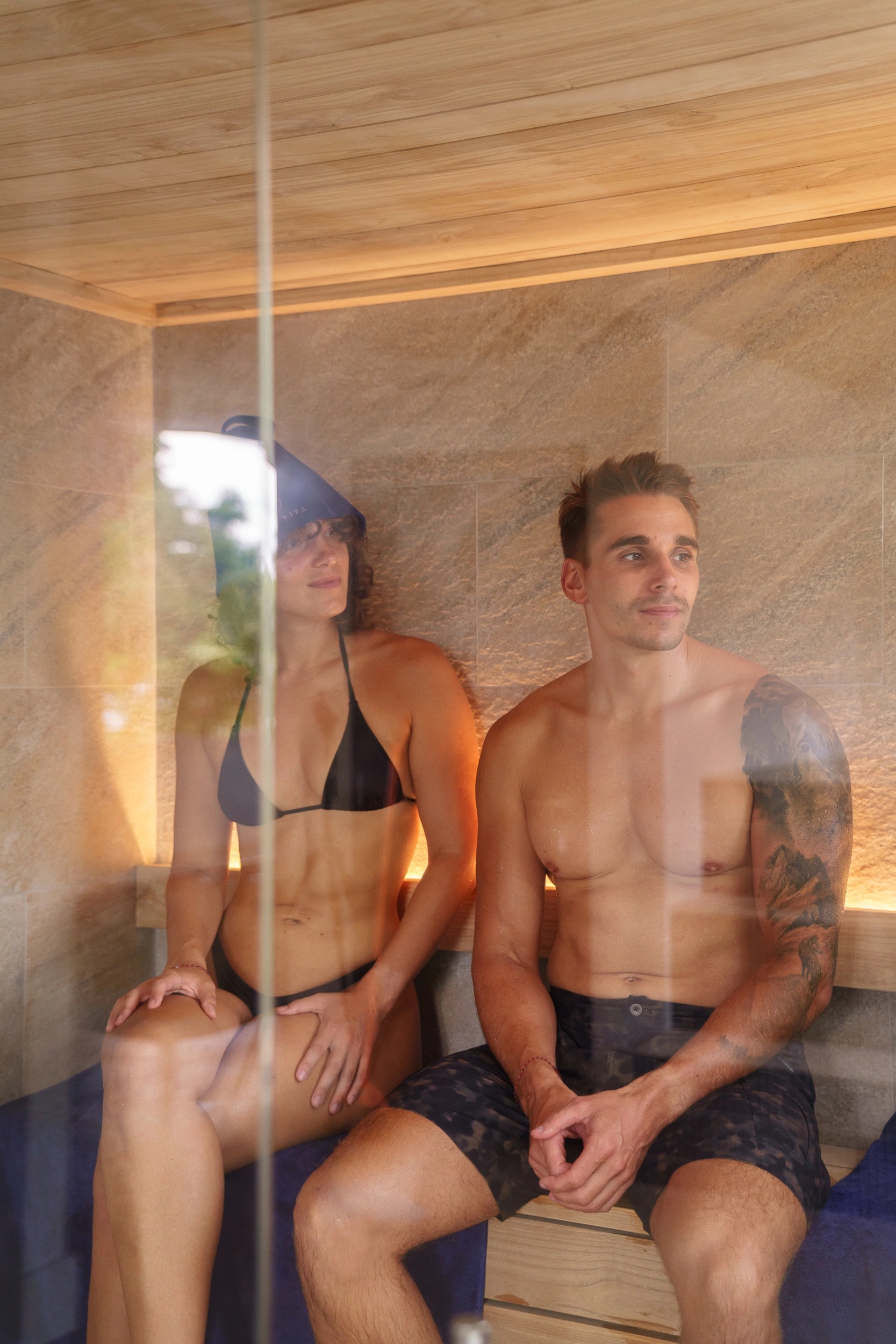 A man and a woman sitting inside a modern wooden sauna room.