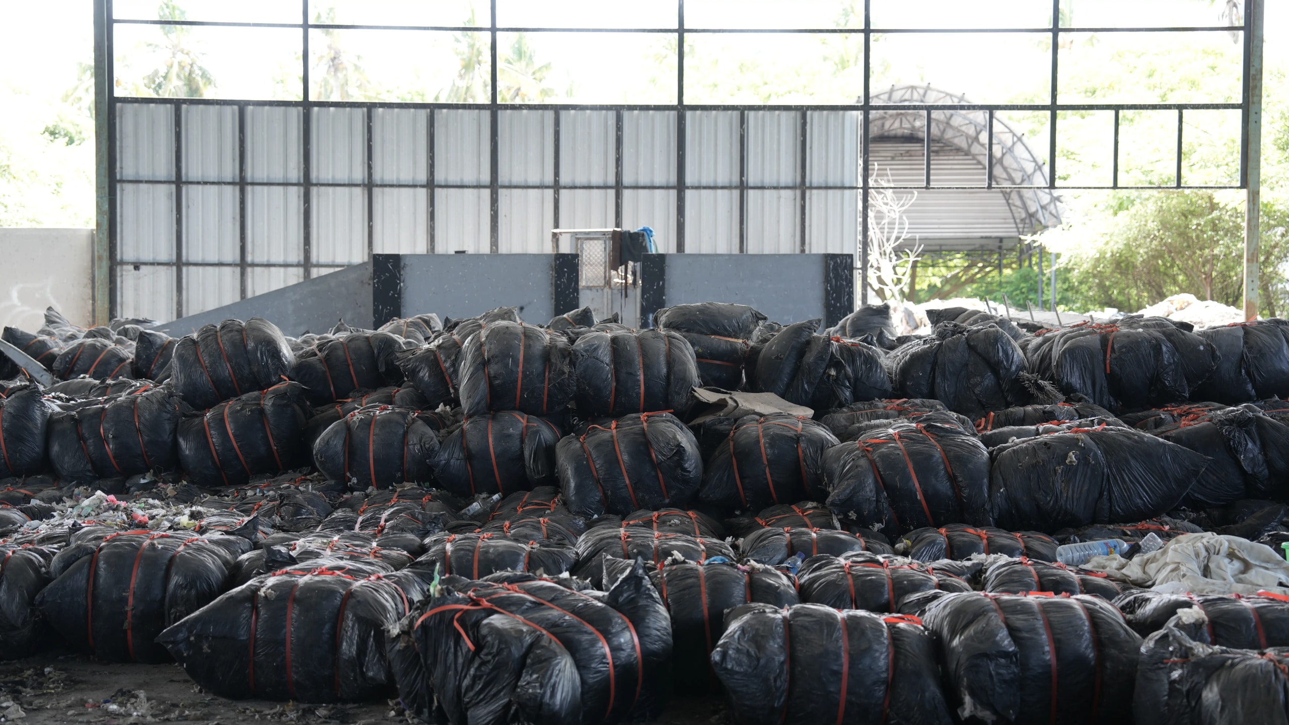 Rows of tightly bound black plastic trash bags piled high inside a warehouse storage facility.