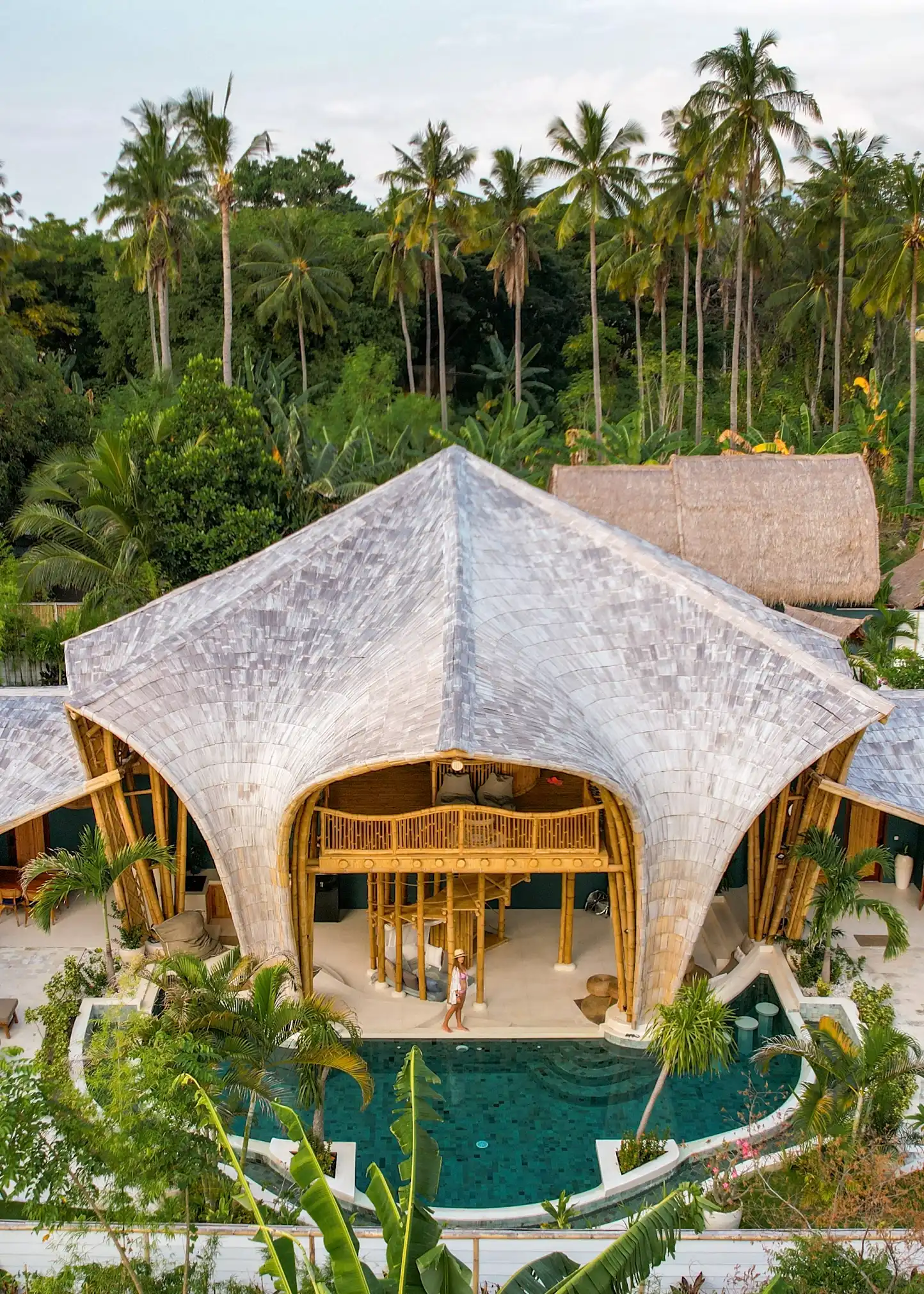 Aerial view of a two-story bamboo villa with a uniquely shaped organic roof and private pool.