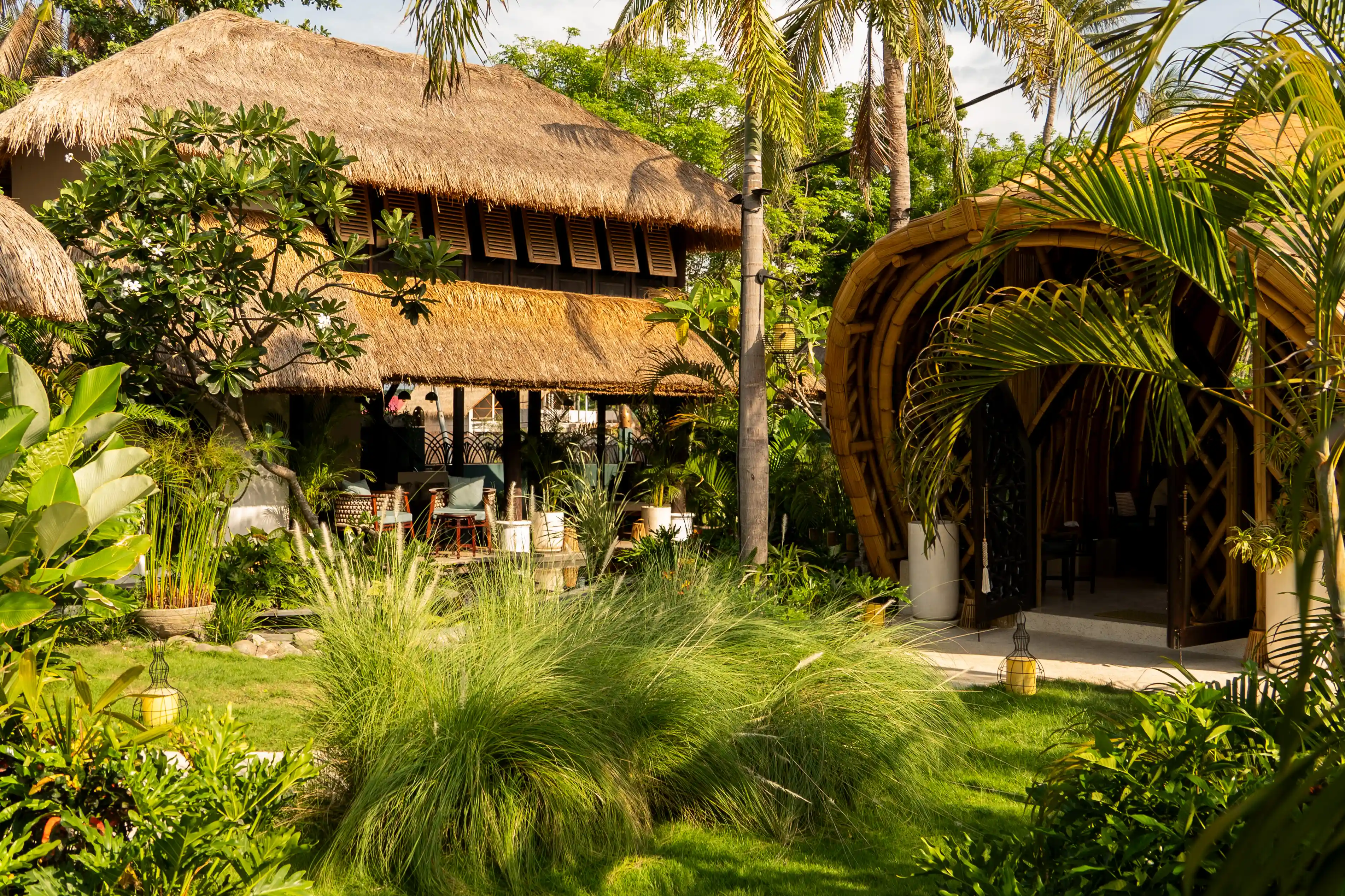 Lush tropical garden surrounding bamboo and thatched-roof resort buildings.