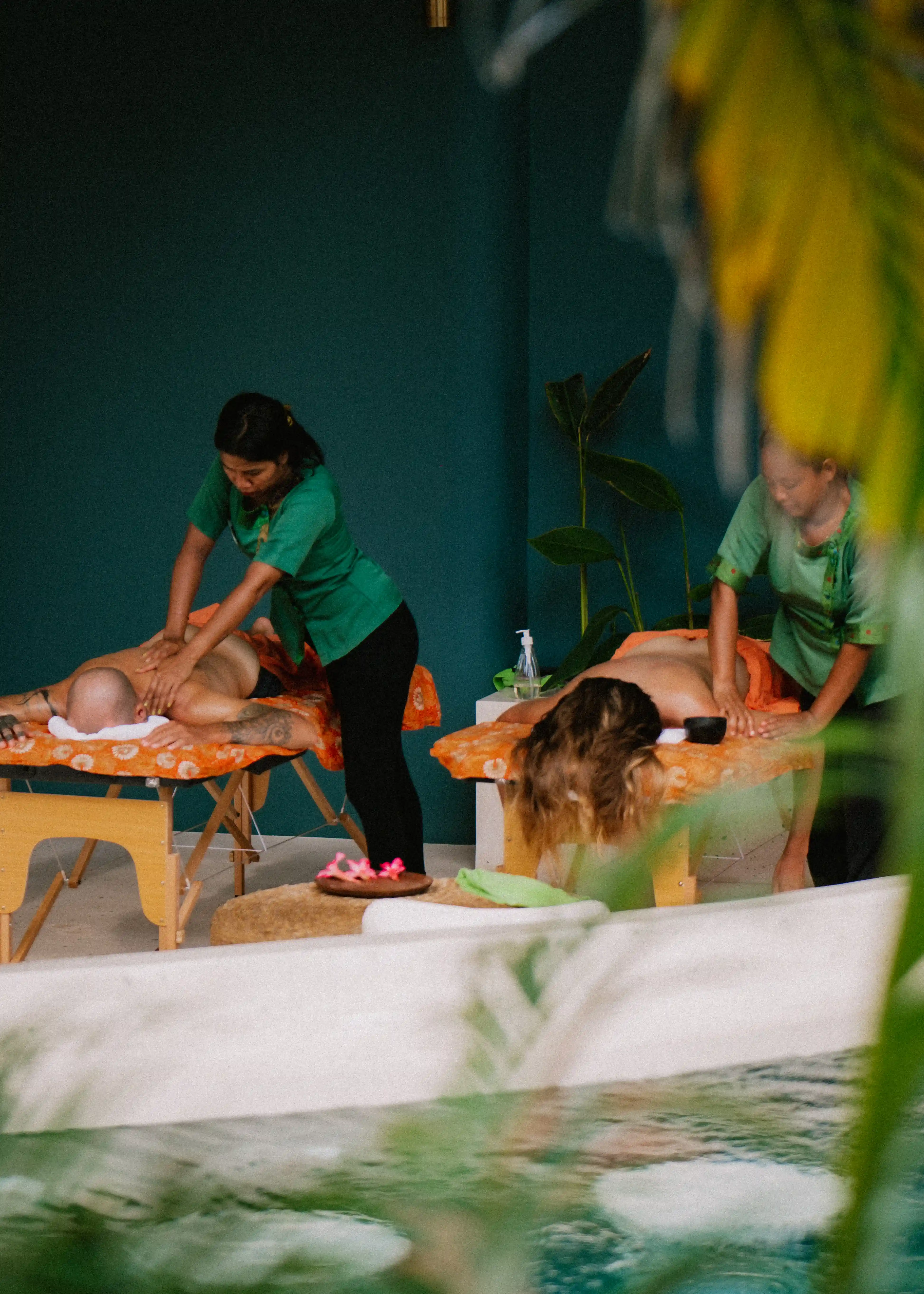 A couple receiving outdoor side-by-side massages from masseuses in an open-air resort setting.