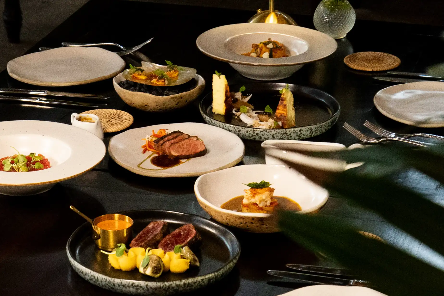 Gourmet dining spread on a dark table featuring various plated dishes and fine dining presentation.